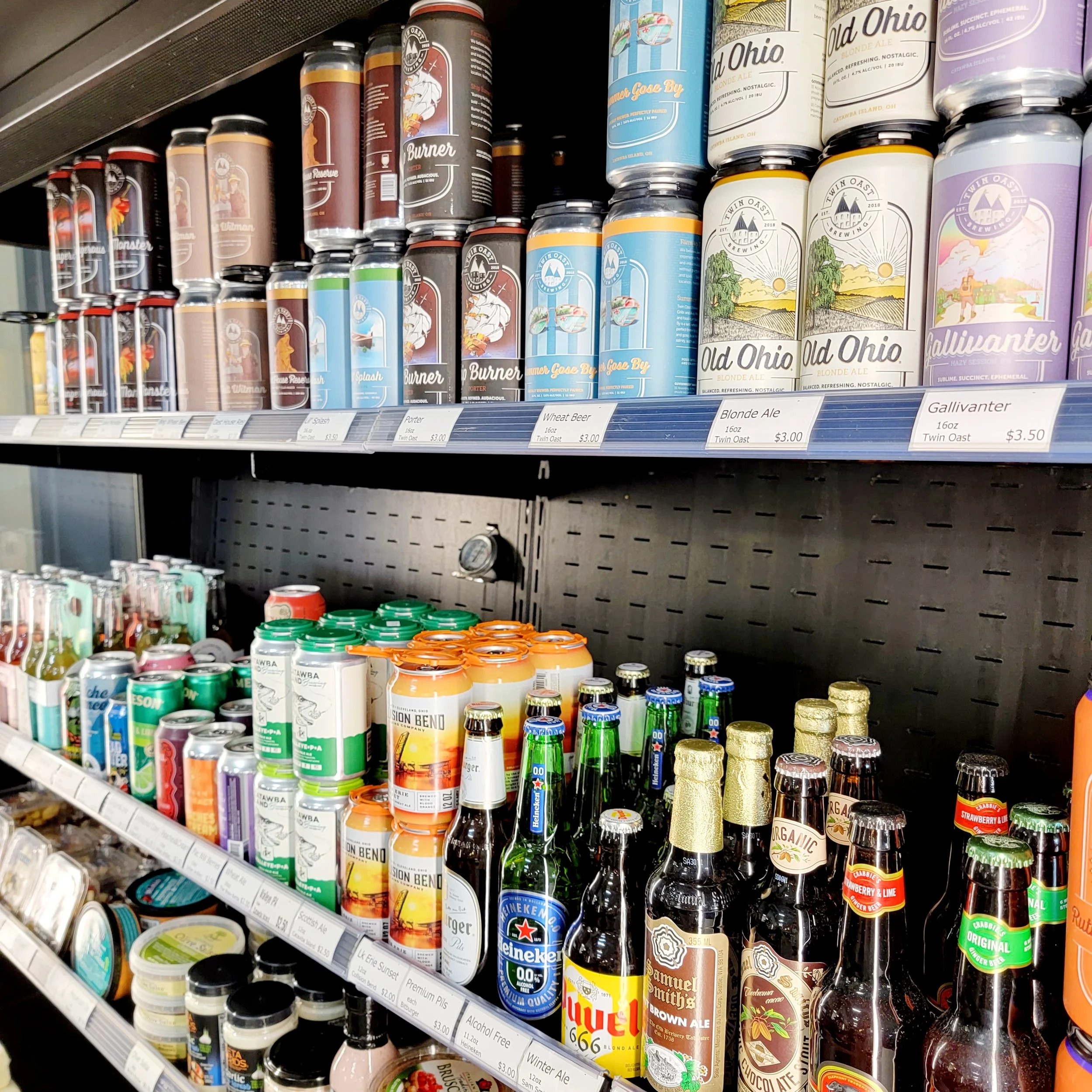 Shelves stocked with various cans and bottles of beer including Old Ohio Blonde Ale, Gallivanter, and Samuel Smith's Brown Ale in a grocery store.