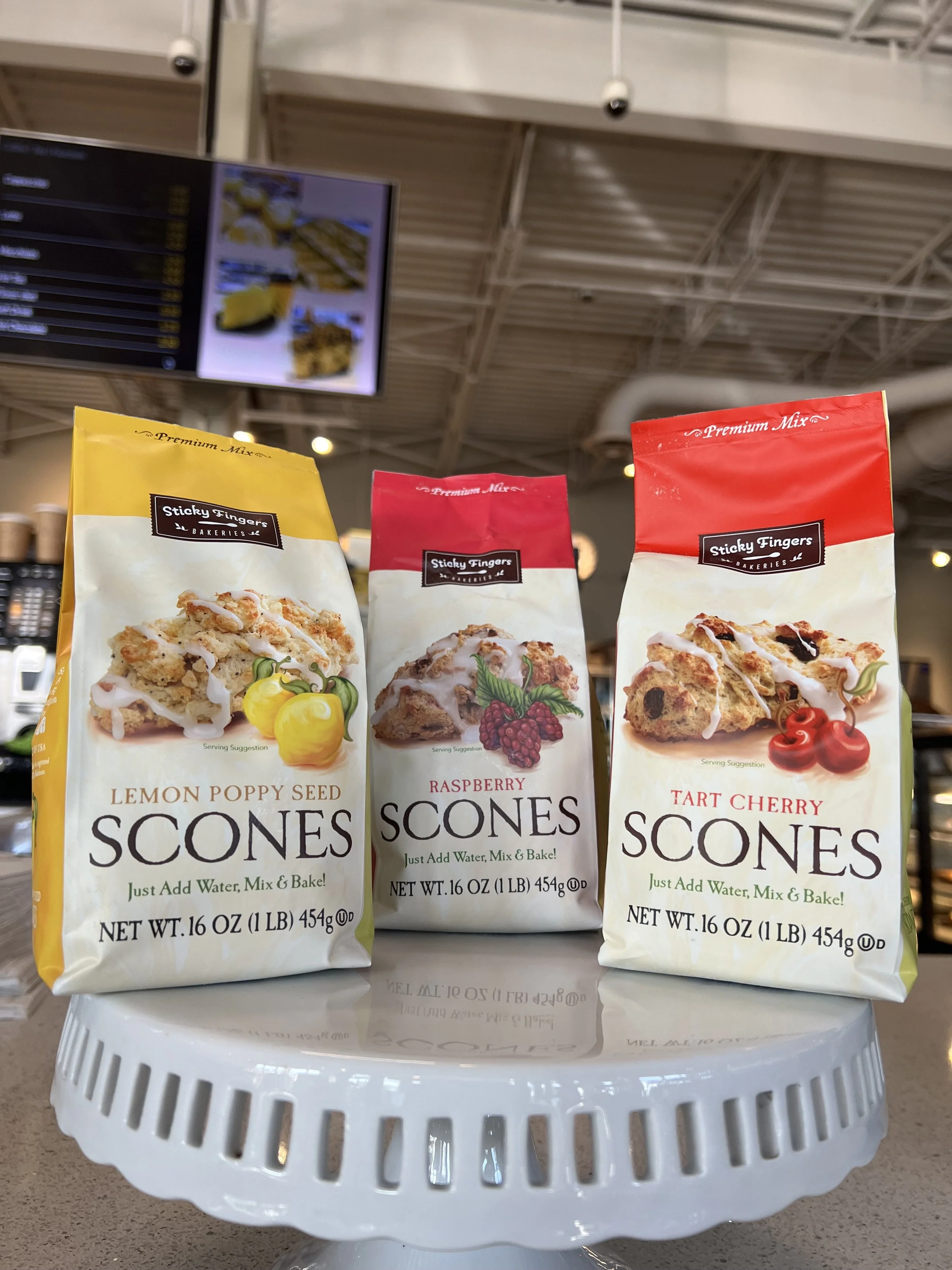 Three bags of scone mixes labeled lemon poppy seed, raspberry, and tart cherry, placed on a white round stand in a store.