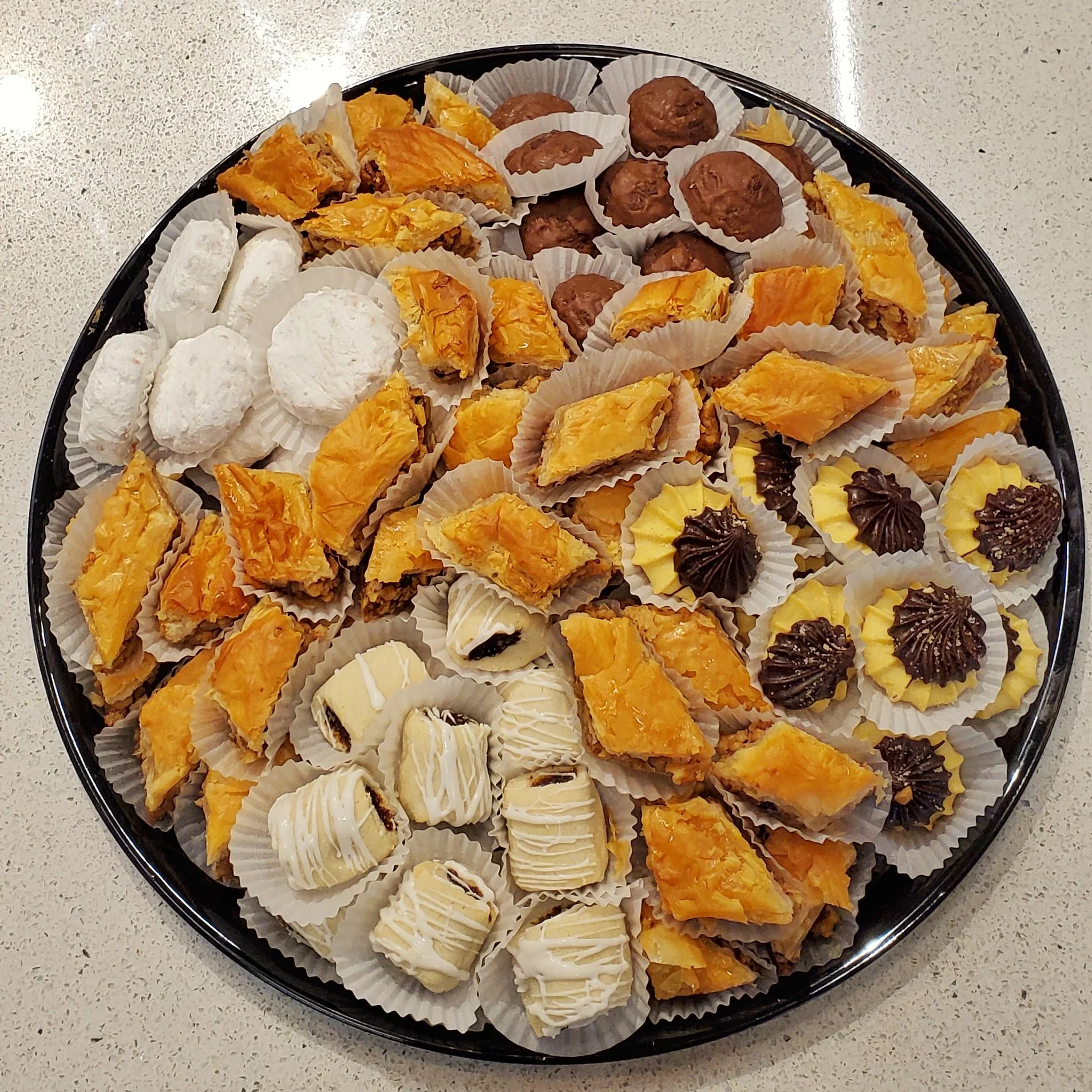 Assorted dessert tray with cookies, pastries, and brownies, arranged in white paper cups on a black round tray.
