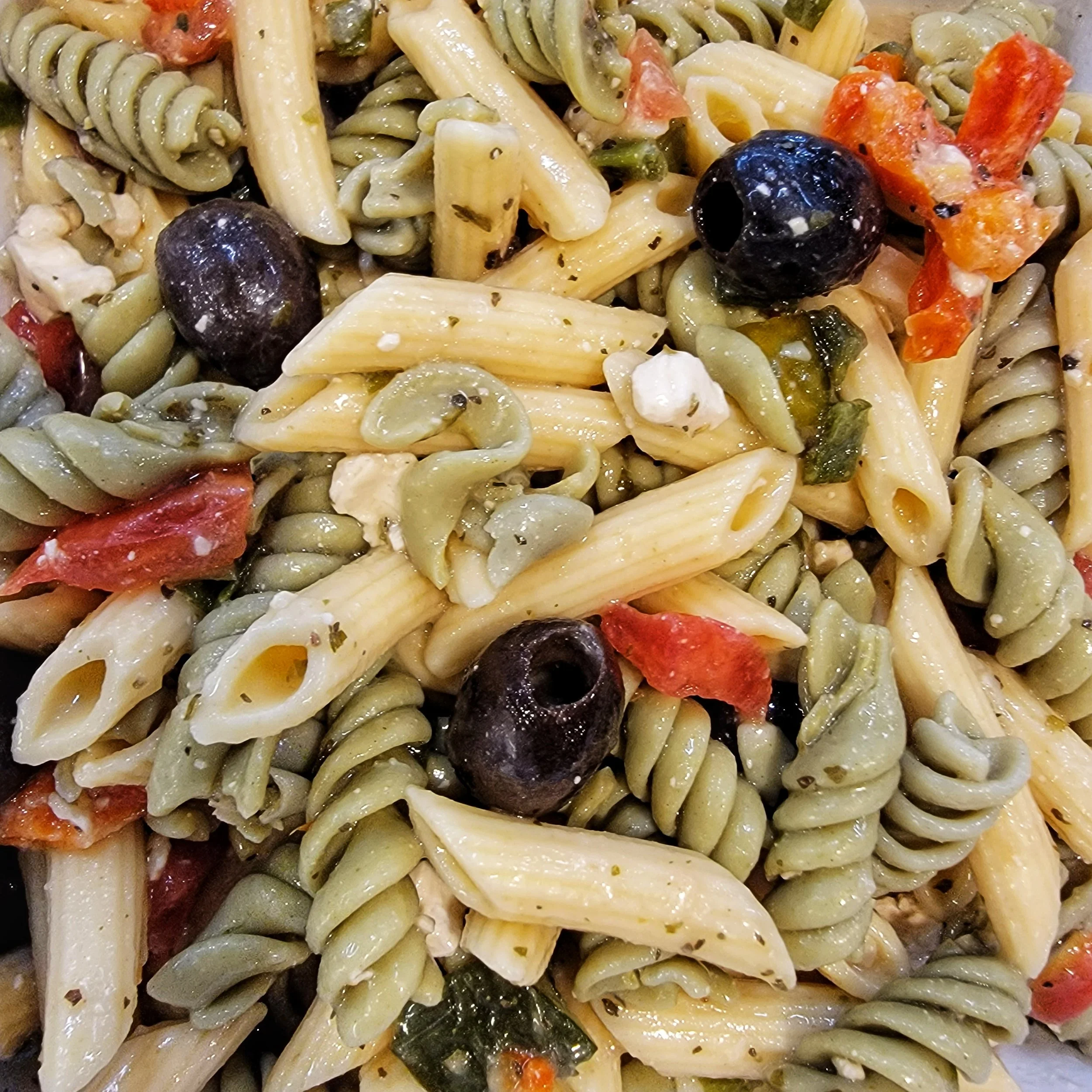 Close-up of a mixed pasta salad with fusilli, penne, cherry tomatoes, black olives, artichoke hearts, and herbs.