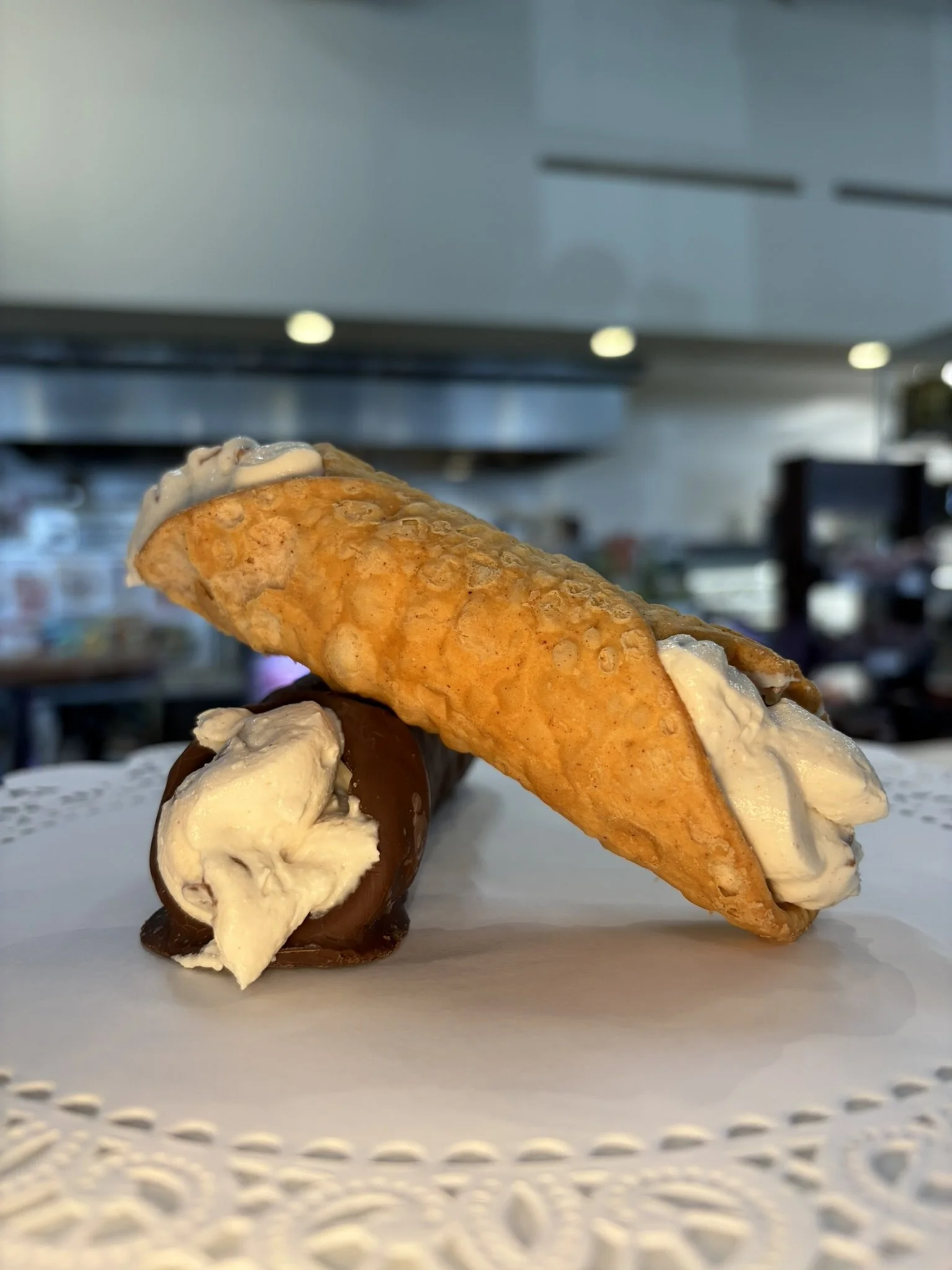 A plate with cannoli pastry topped with chocolate syrup, filled with sweet filling, set on a white table in a restaurant.