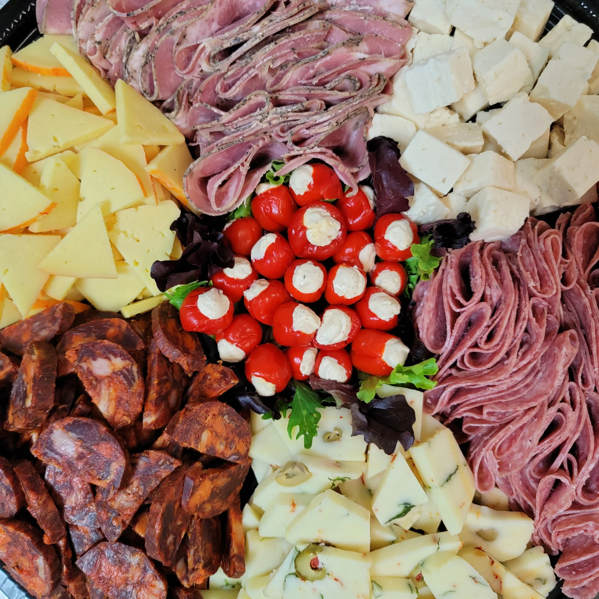 A close-up of a cheese and charcuterie platter featuring various cheeses, cured meats, cherry tomatoes, and greens.