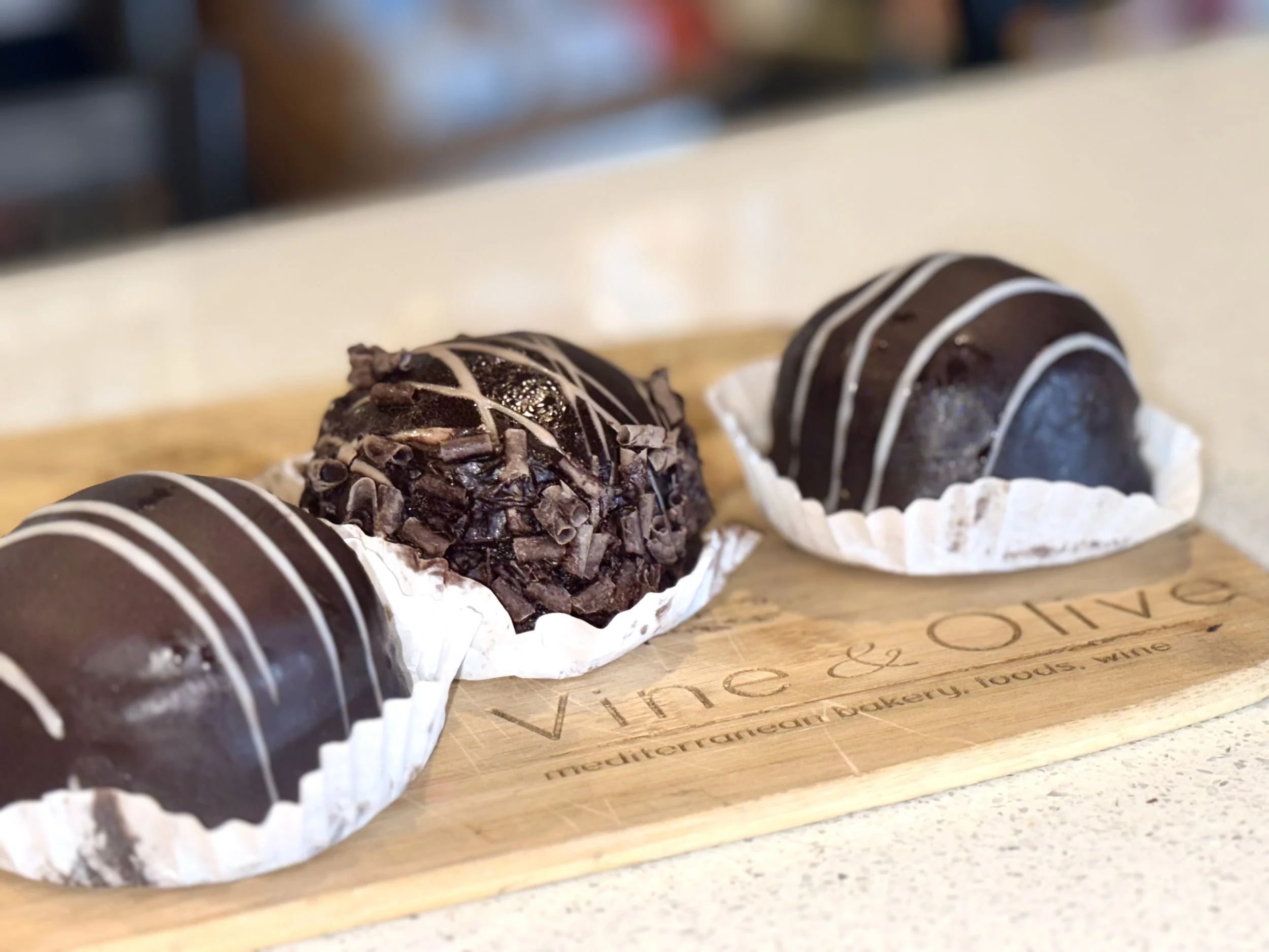Assorted chocolate truffles decorated with white drizzle and chocolate shavings on a wooden board.