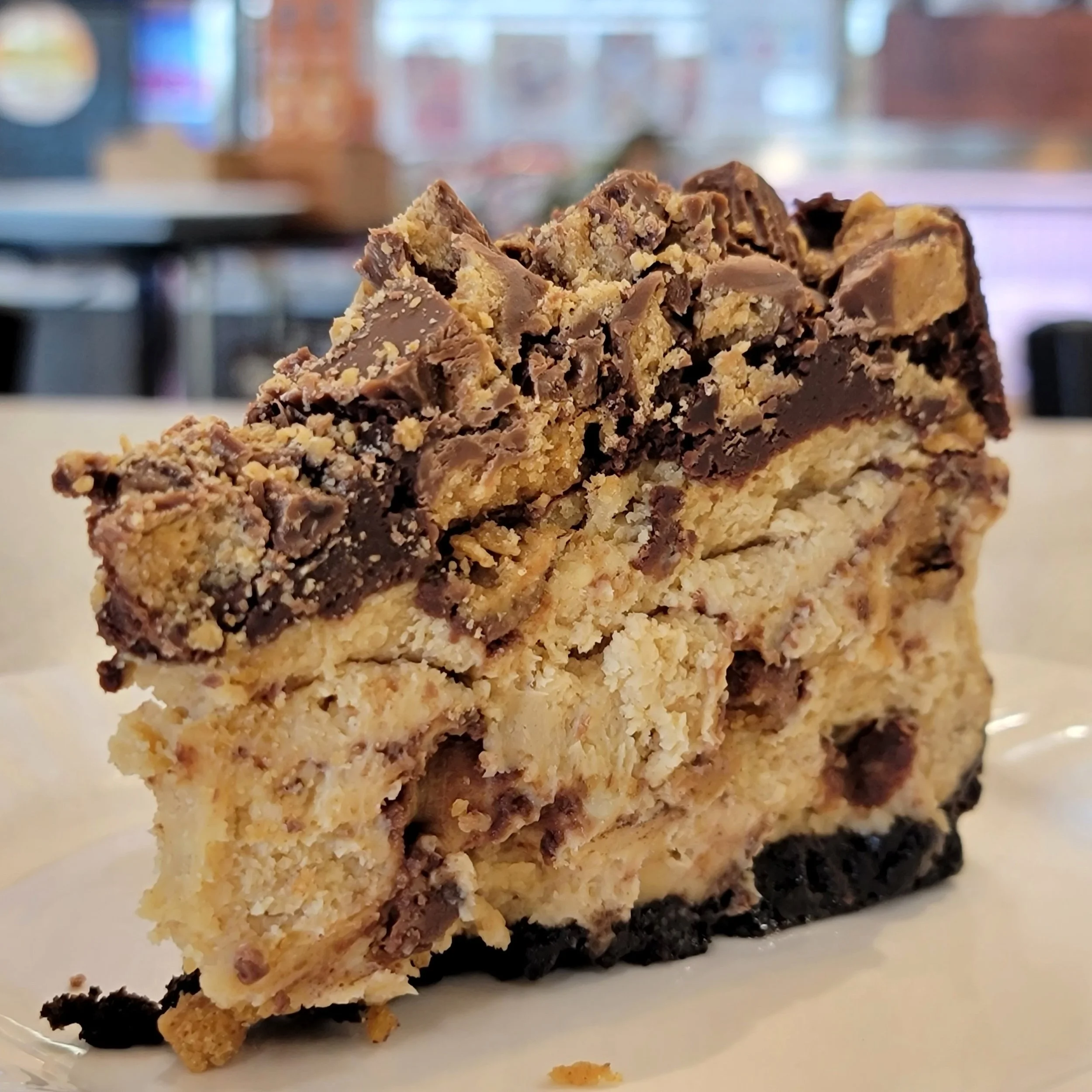 Close-up of a crumbly chocolate and peanut butter cheesecake with layers of chocolate and peanut butter filling, on a white plate.