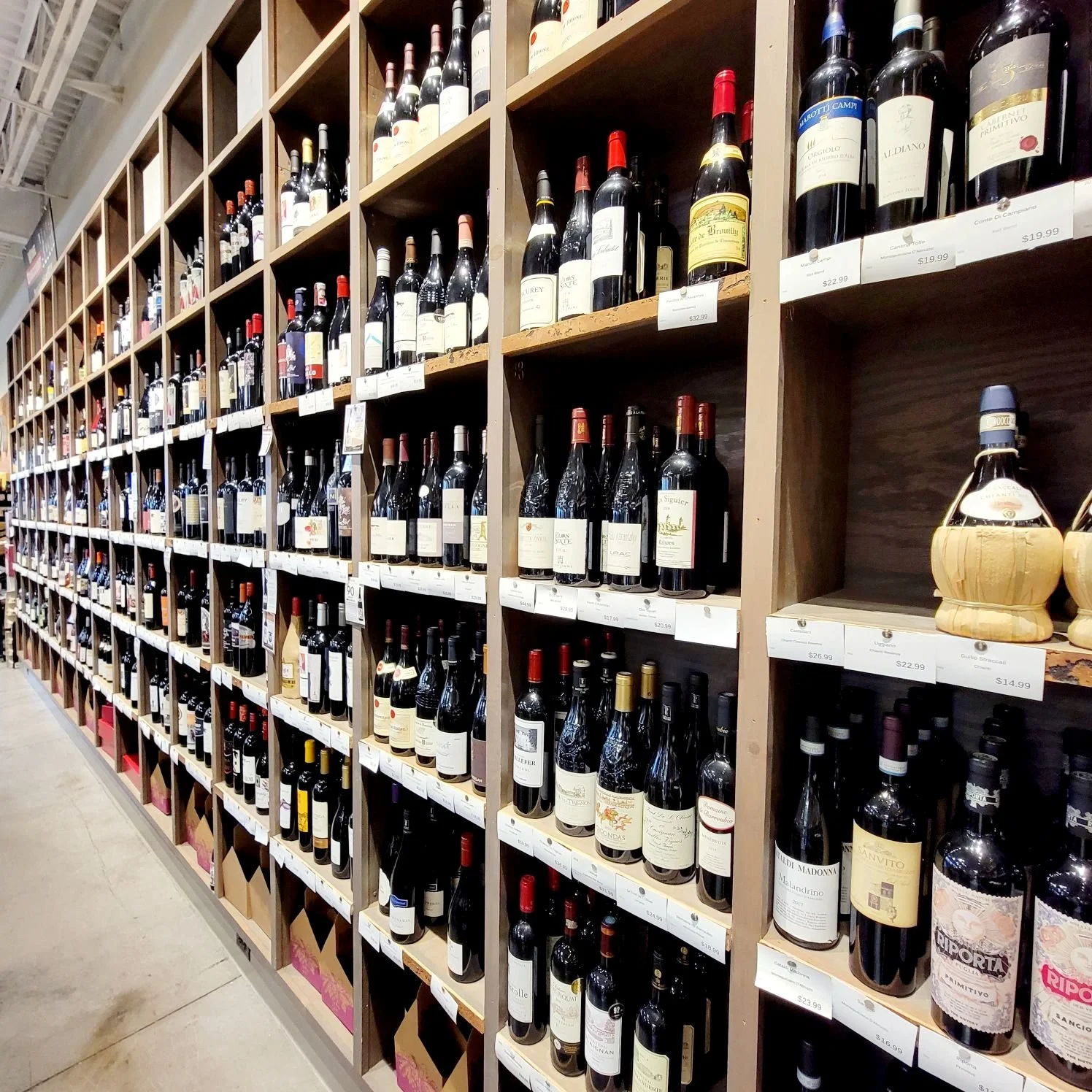 Shelves of various bottles of red wine in a store, with price tags displayed underneath.