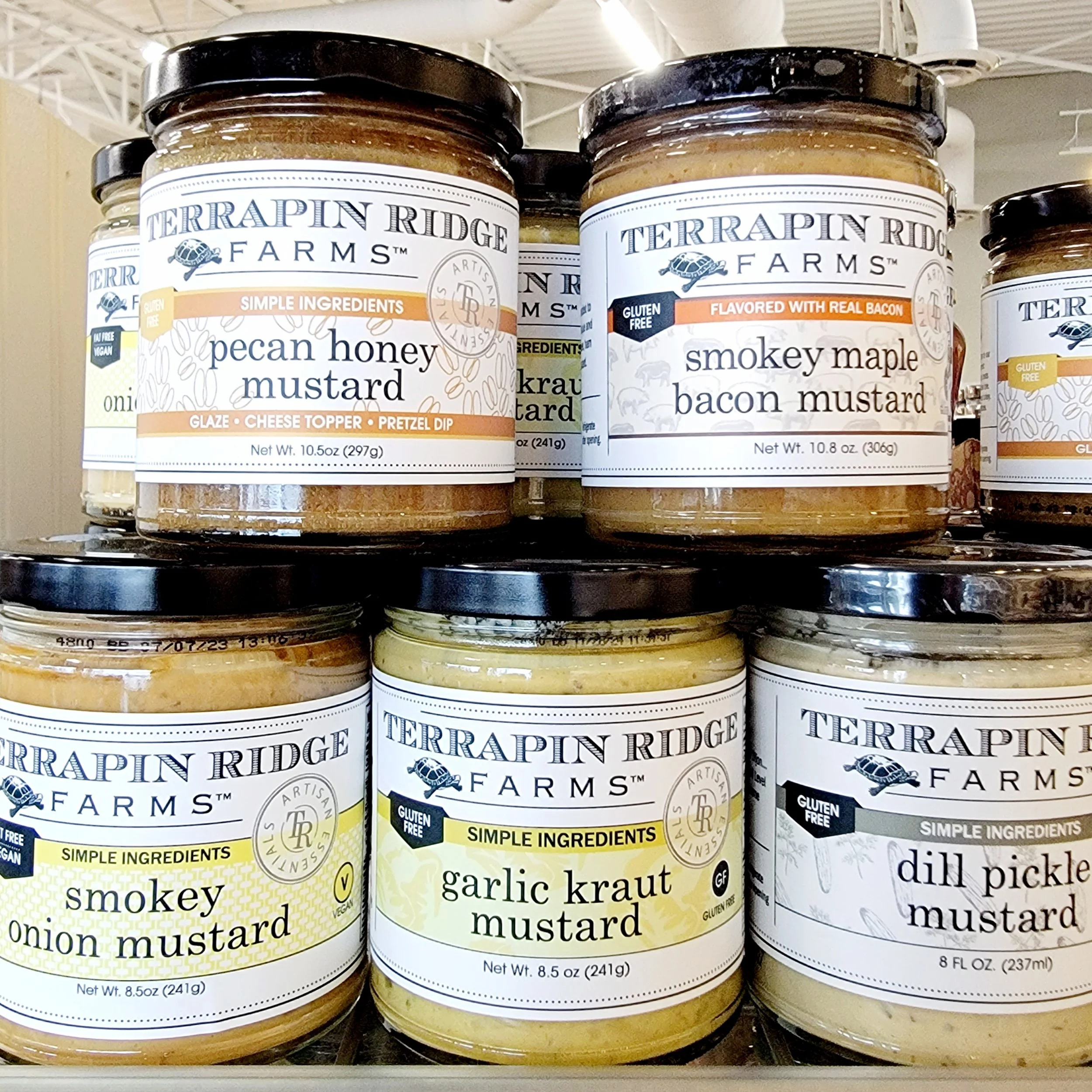 Several jars of Terrapin Ridge Farms mustard flavors, including pecan honey mustard, garlic kraut mustard, smoky maple bacon mustard, and dill pickle mustard, are displayed on store shelves.