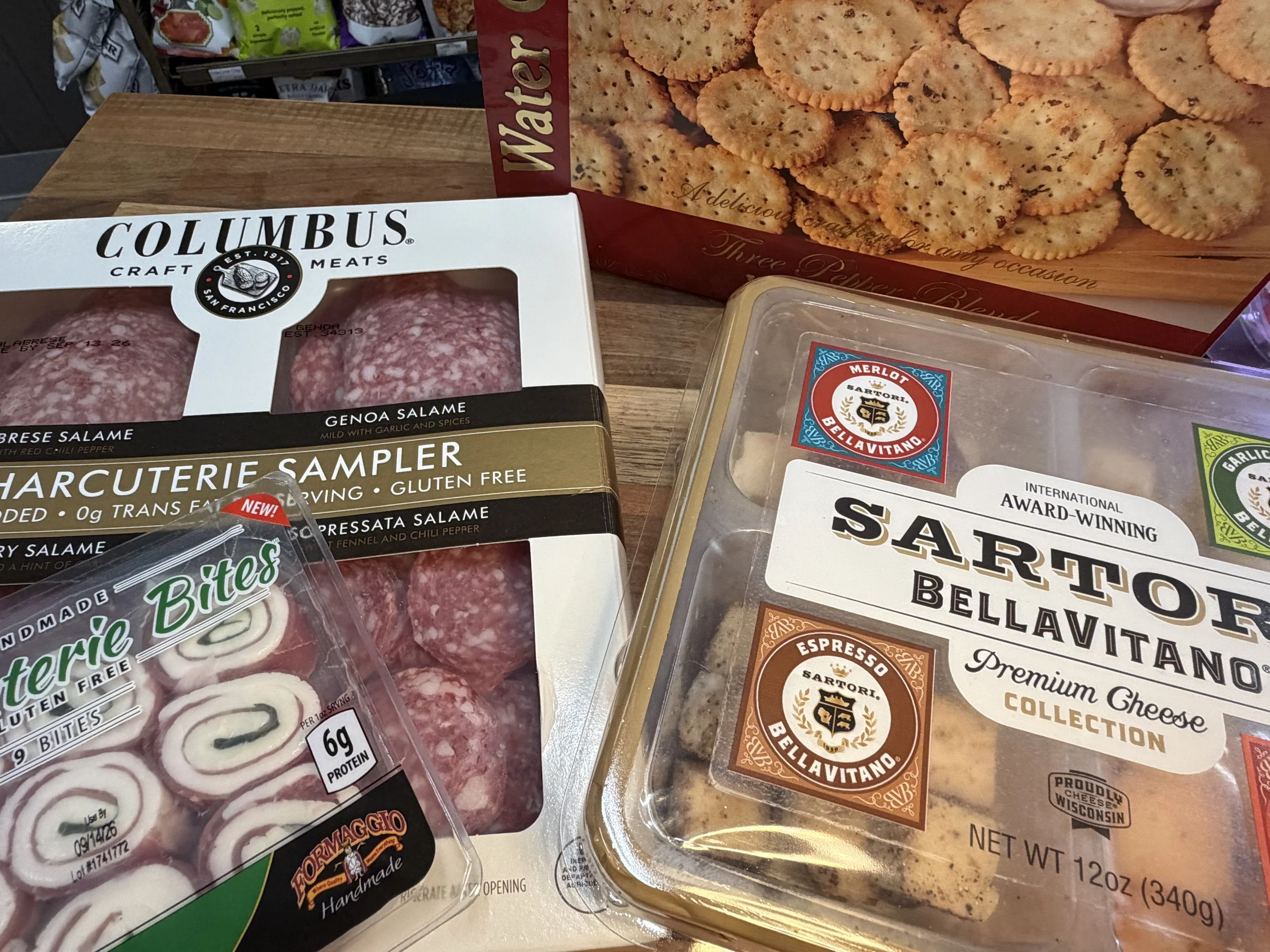 Assorted packaged meats including salami, and a tray of crackers on a wooden surface.