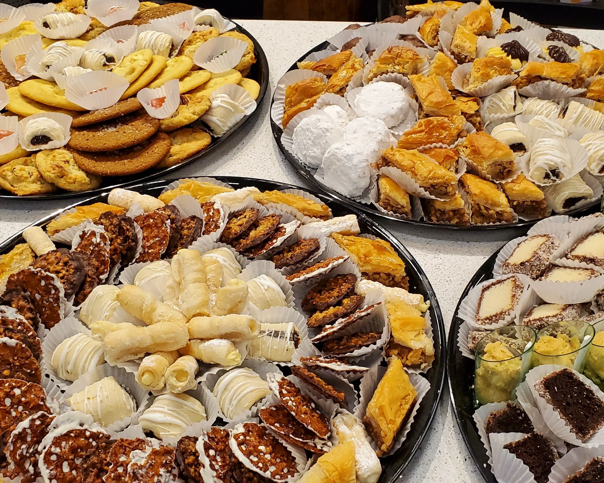 Assorted bakery treats including cookies, pastries, and confections displayed on black trays lined with white paper cups.