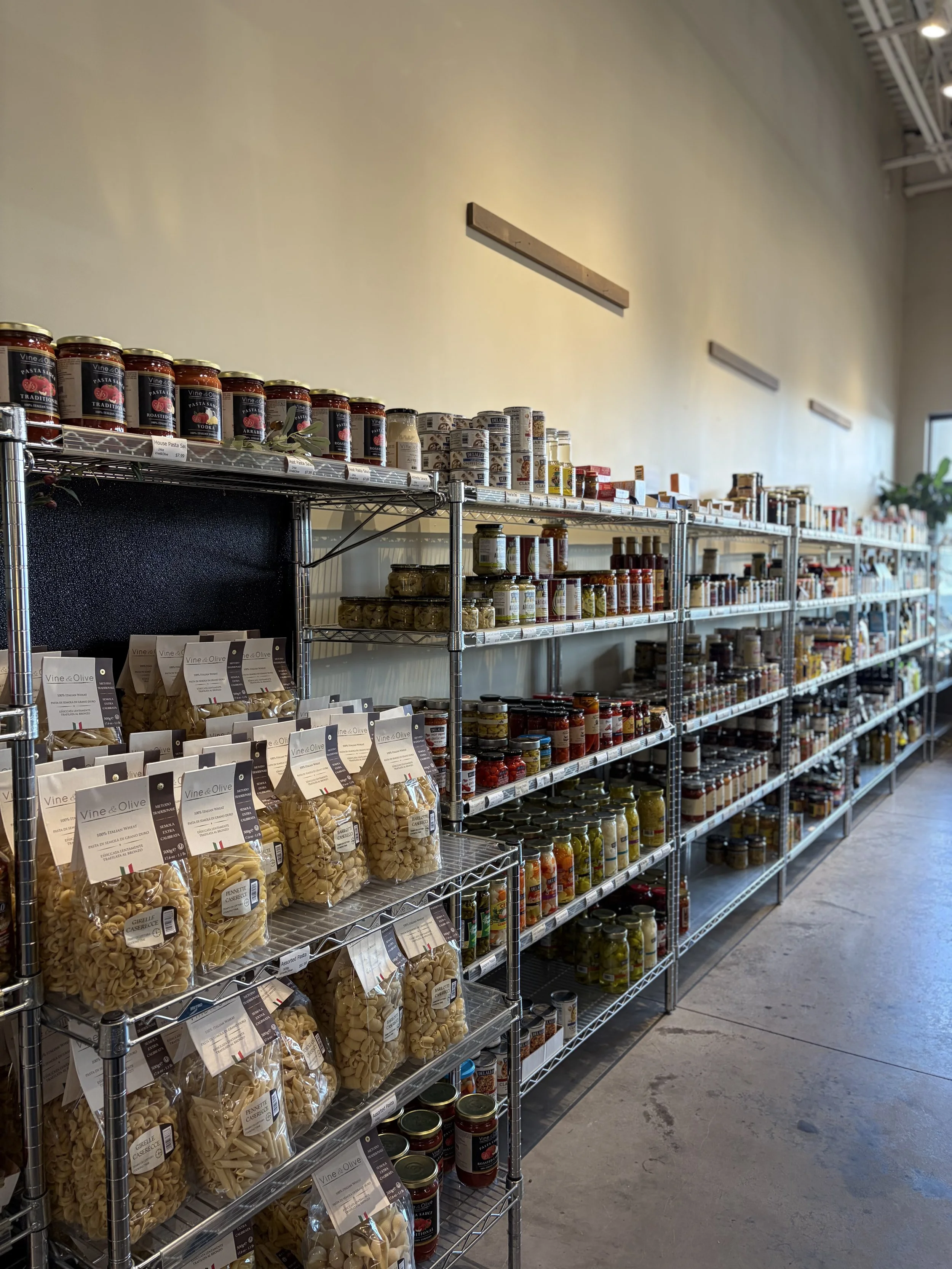 Store aisle with metal shelves stocked with jars and packages of pasta, sauces, and food products.