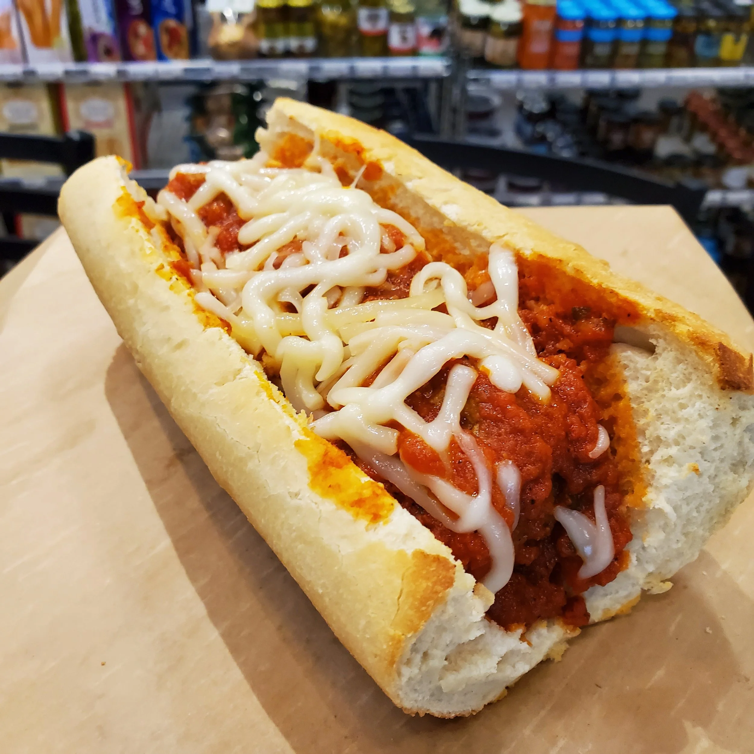 Close-up of hot sandwich with cheese, sauce, and toppings, on a piece of parchment paper in a grocery store.