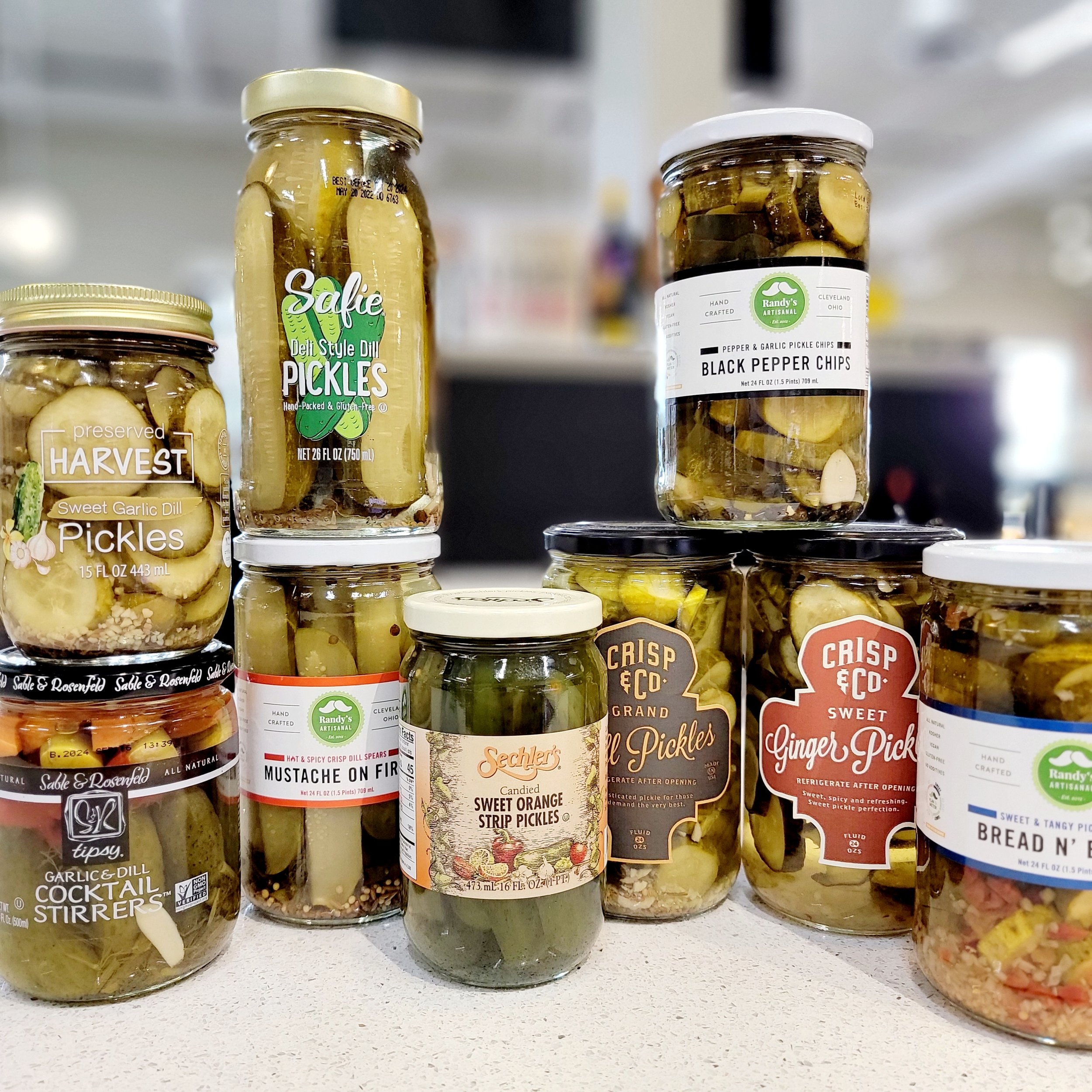 Glass jars filled with olives, pickles and peppers on a store shelf.