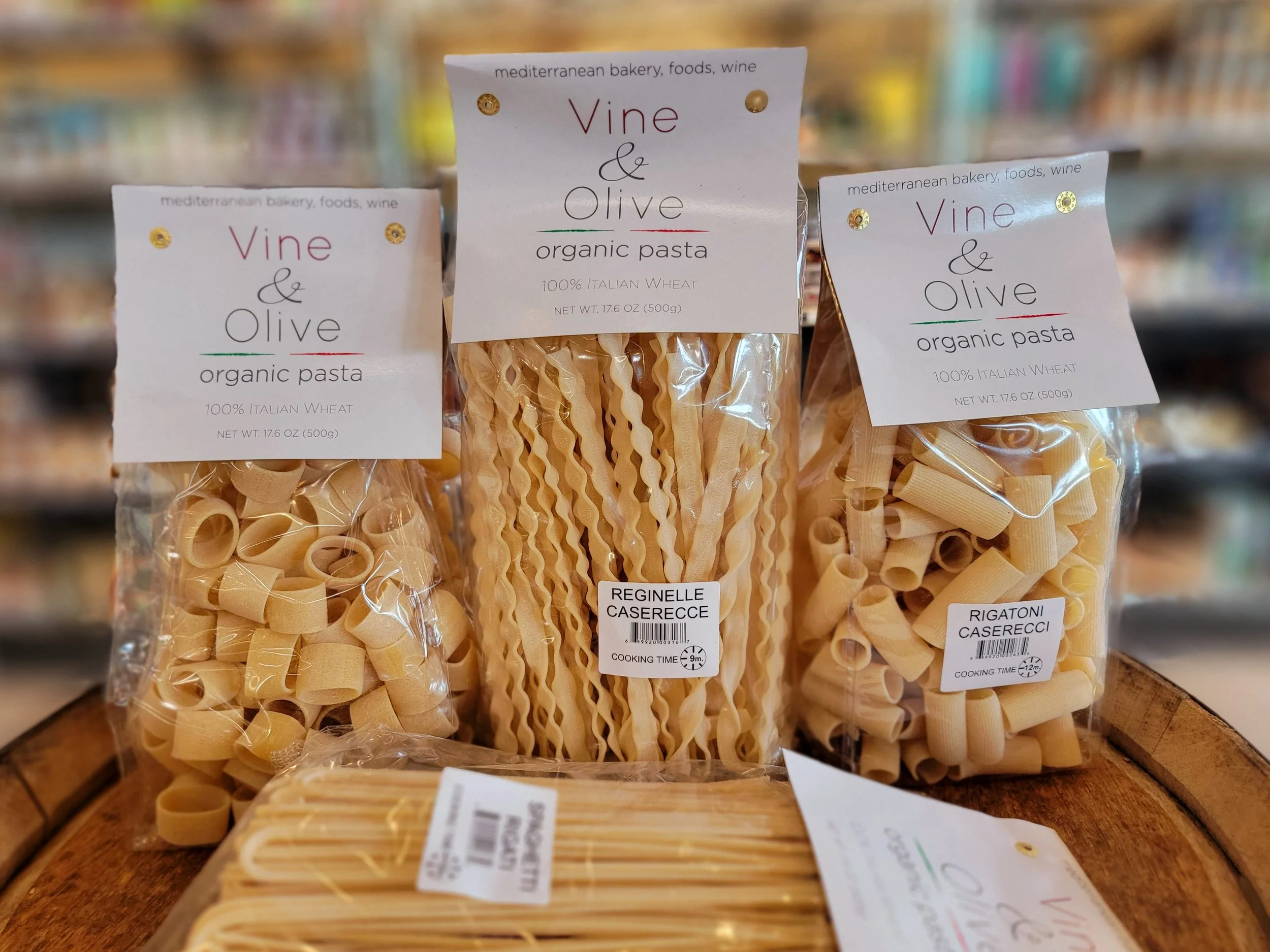 Three packages of organic pasta from Vina & Olive on a wooden surface, with blurred background of a store shelf.