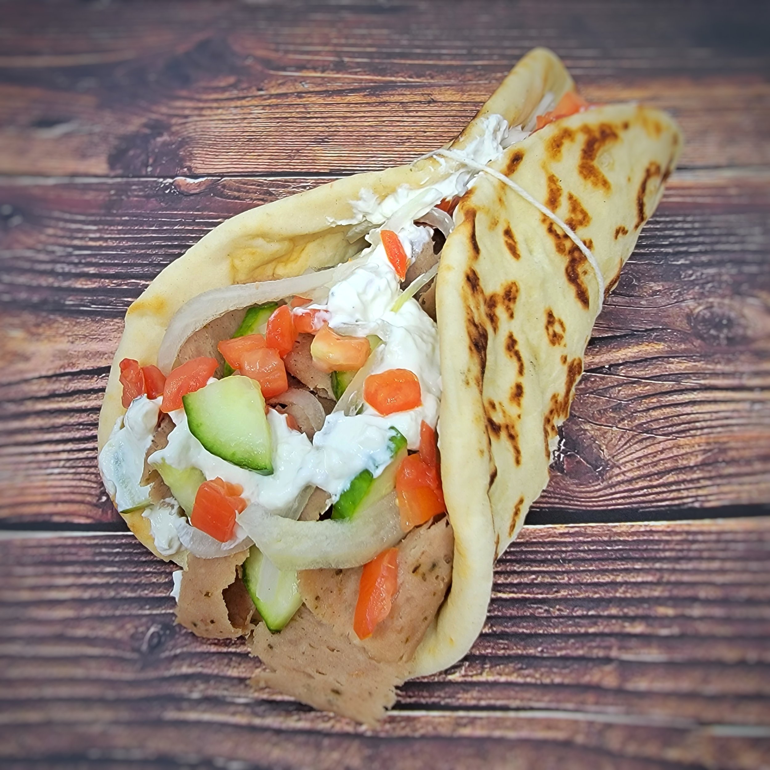 A gyro with flatbread filled with chopped vegetables, sour cream, and lamb or chicken, placed on a wooden surface.