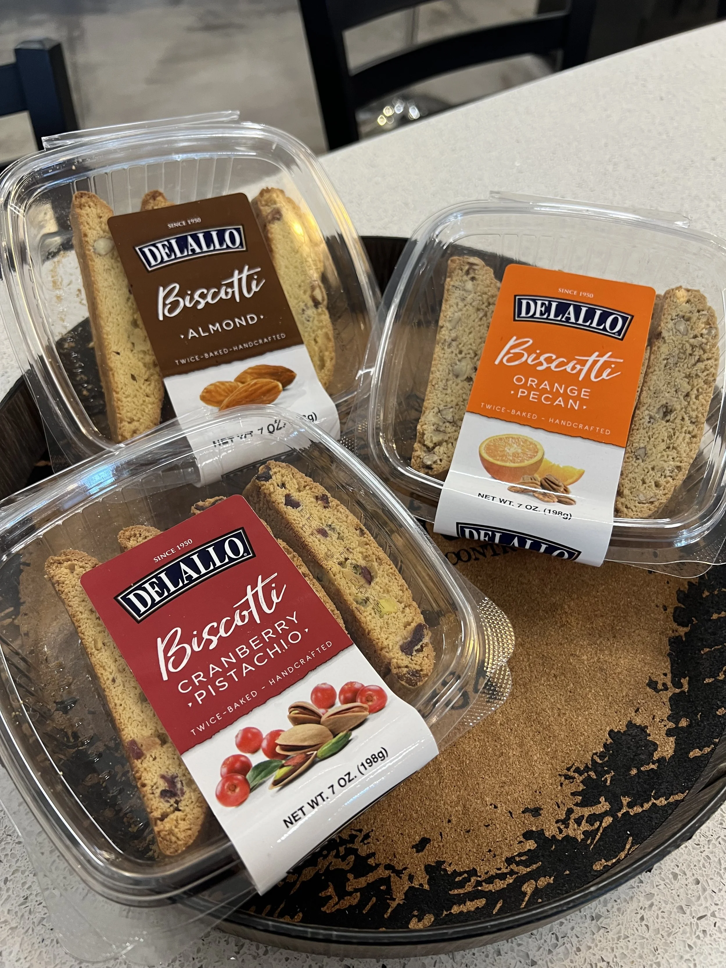 Multiple packages of DeLallo Biscotti on a table, including almond, orange pecan, and cranberry pistachio flavors.