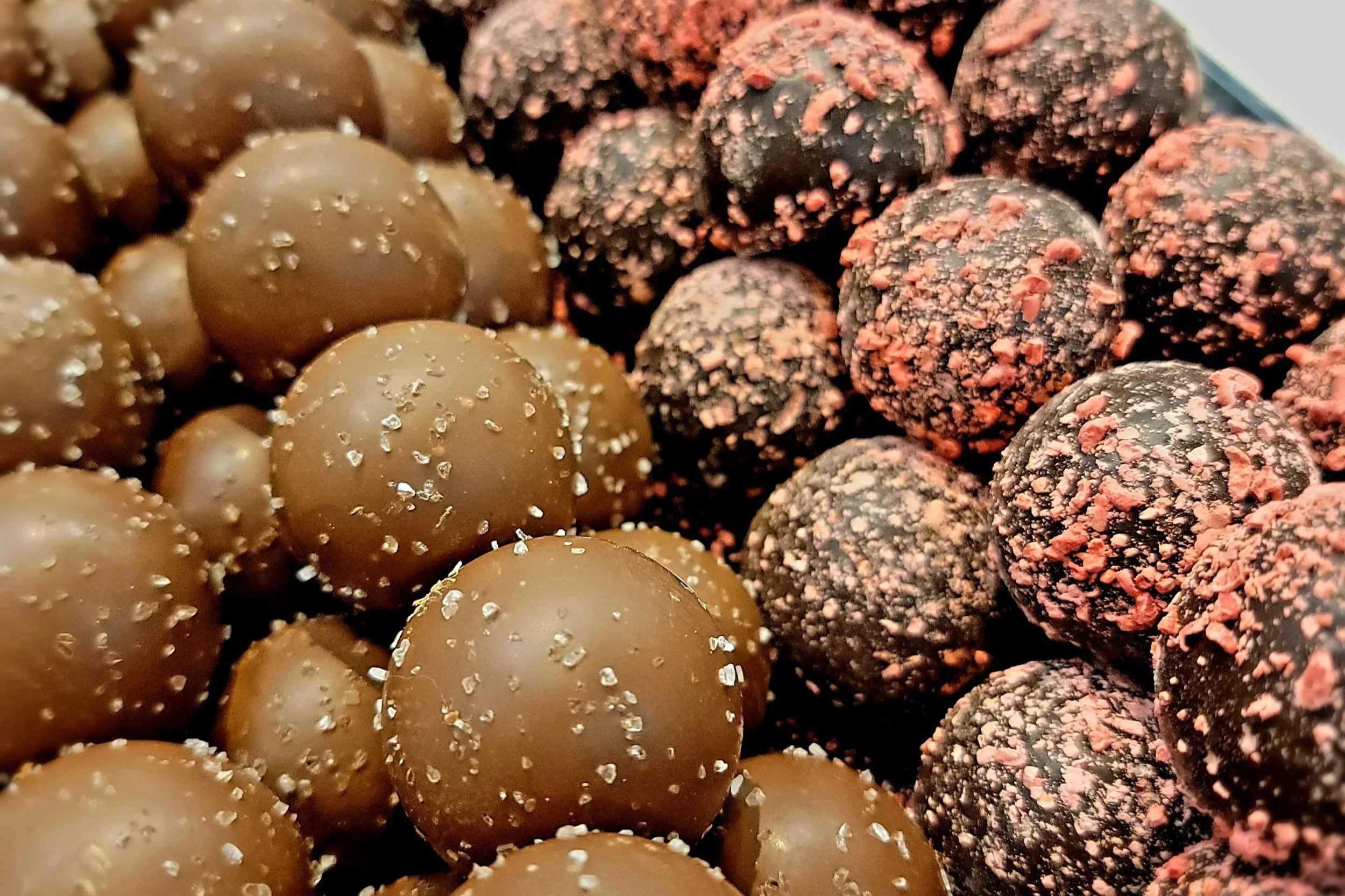 Close-up of assorted truffles with various toppings and coatings, including sea salt and crushed pink peppercorns.