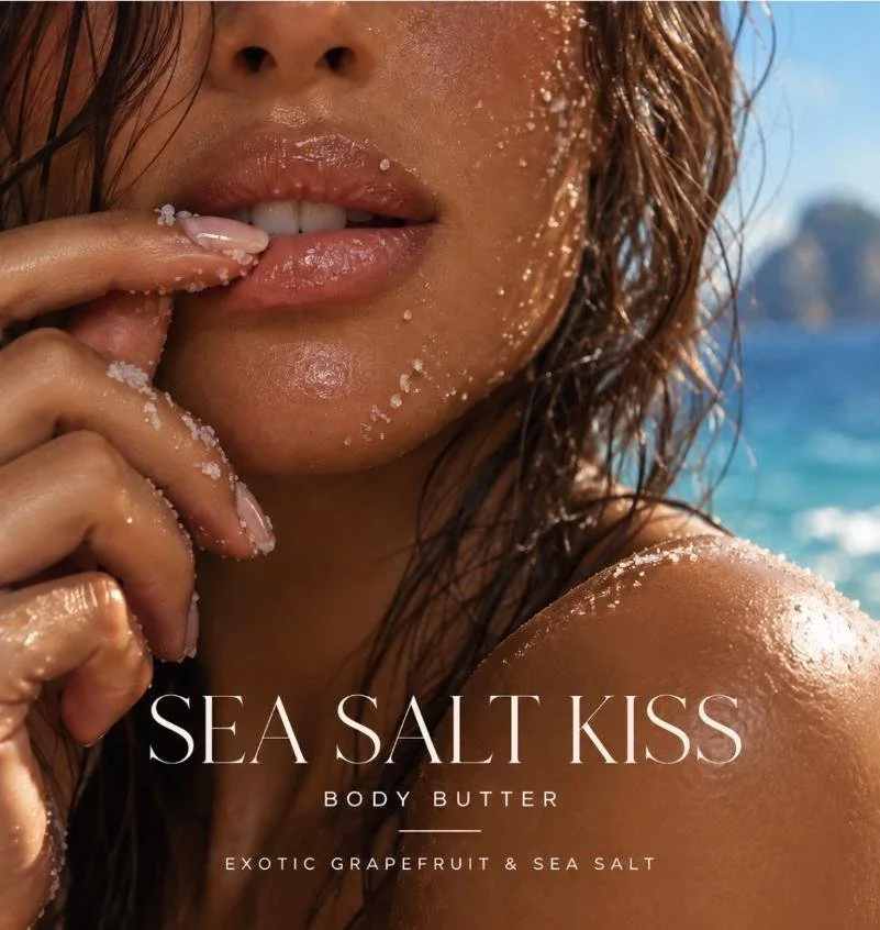 Close-up of a woman with wet hair applying sea salt body butter with exfoliating sea salt on her shoulder, near the ocean.
