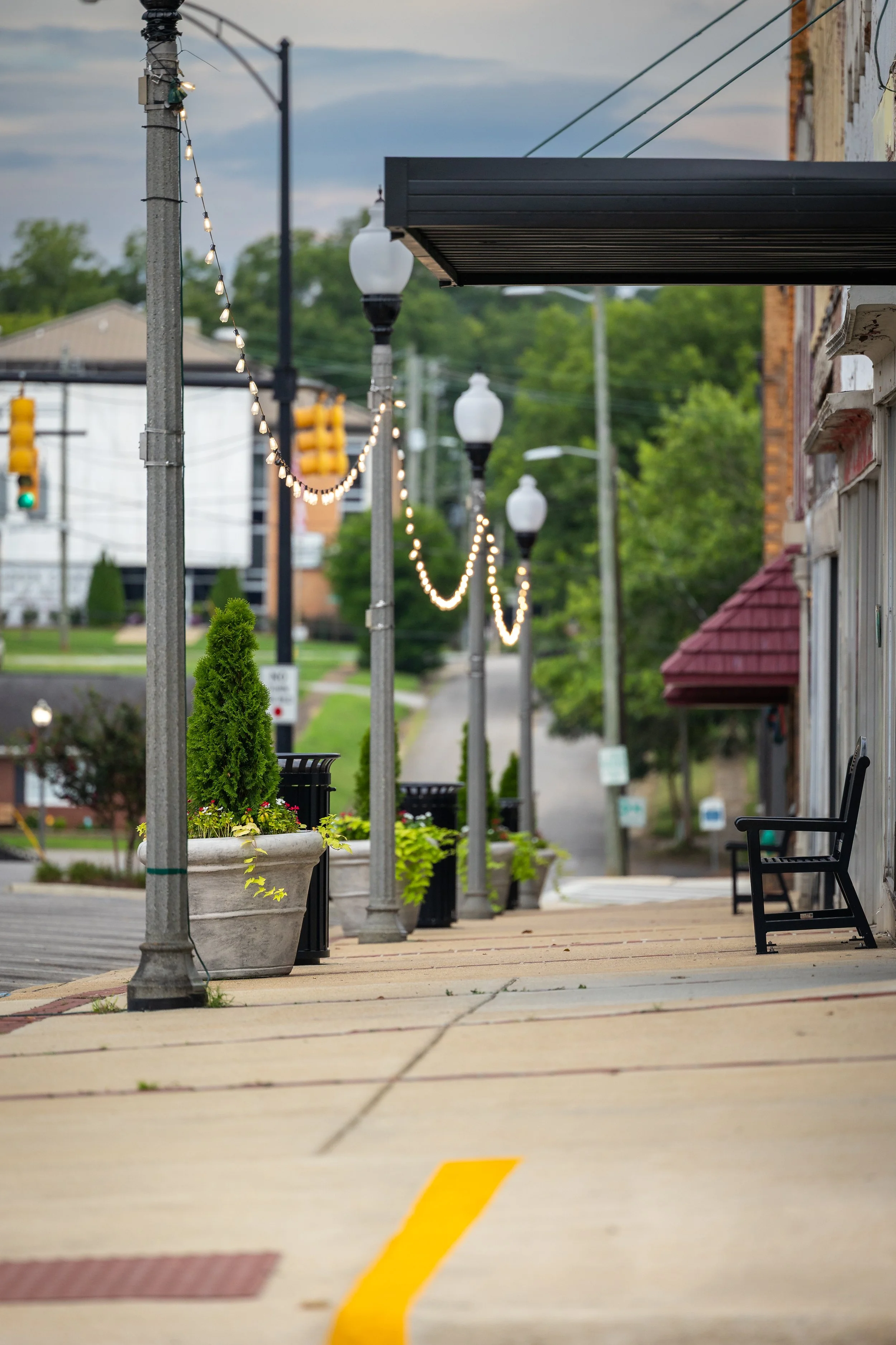 Historic downtown Talladega streetscape featuring decorative planters, lamp posts, and string lights.