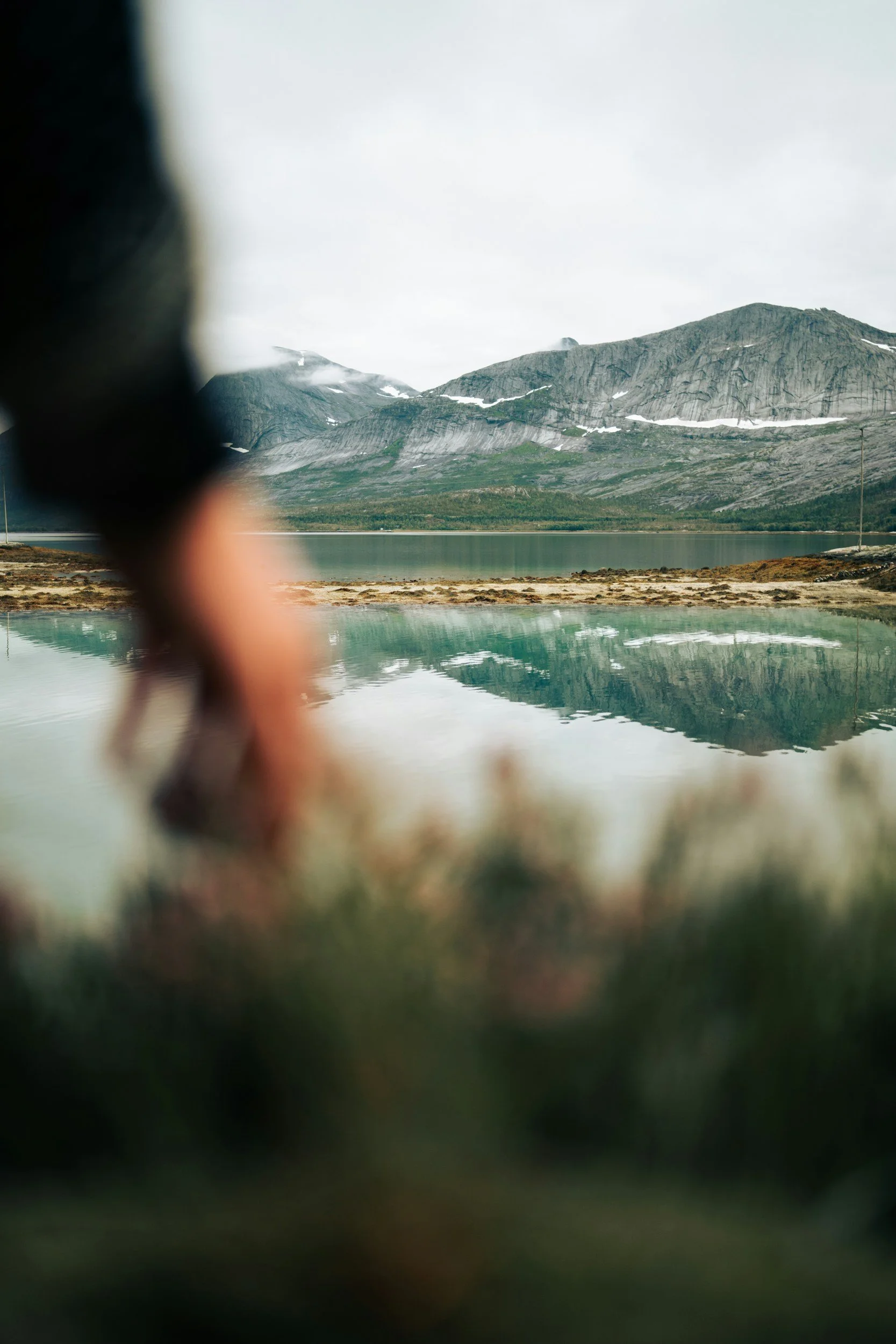 Blurry photo of a mountain landscape with cloudy sky, a body of water in the foreground, and rocky terrain.