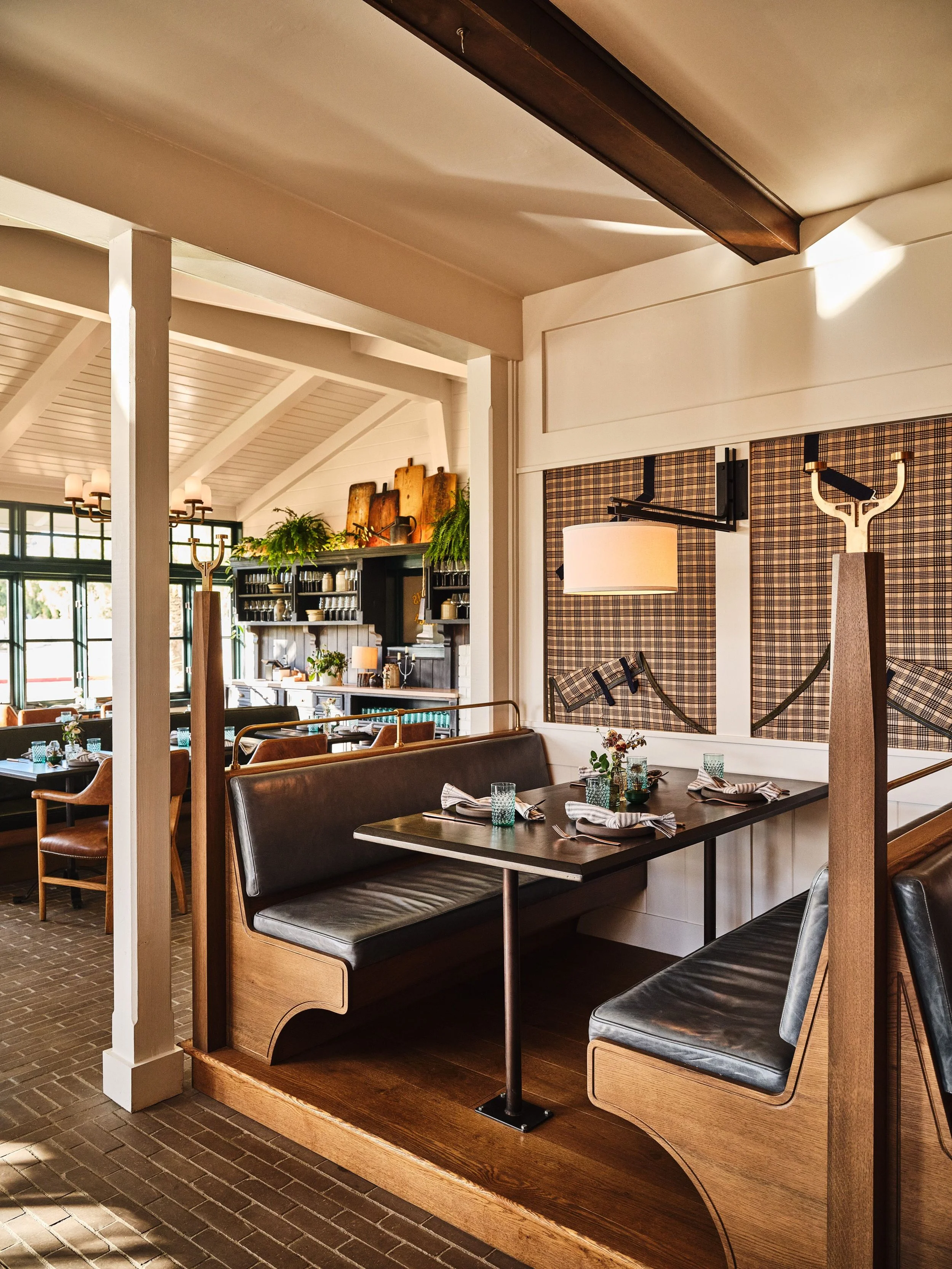 Interior dining area of a restaurant with wooden decor, tables set with napkins and glassware, and a wall with patterned fabric and wall-mounted lamps.