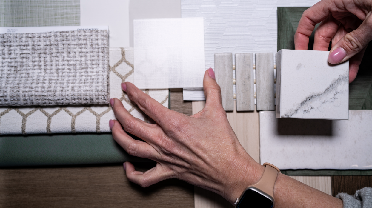 A person's hand arranging tile samples of various colors and textures on a surface for interior design planning.