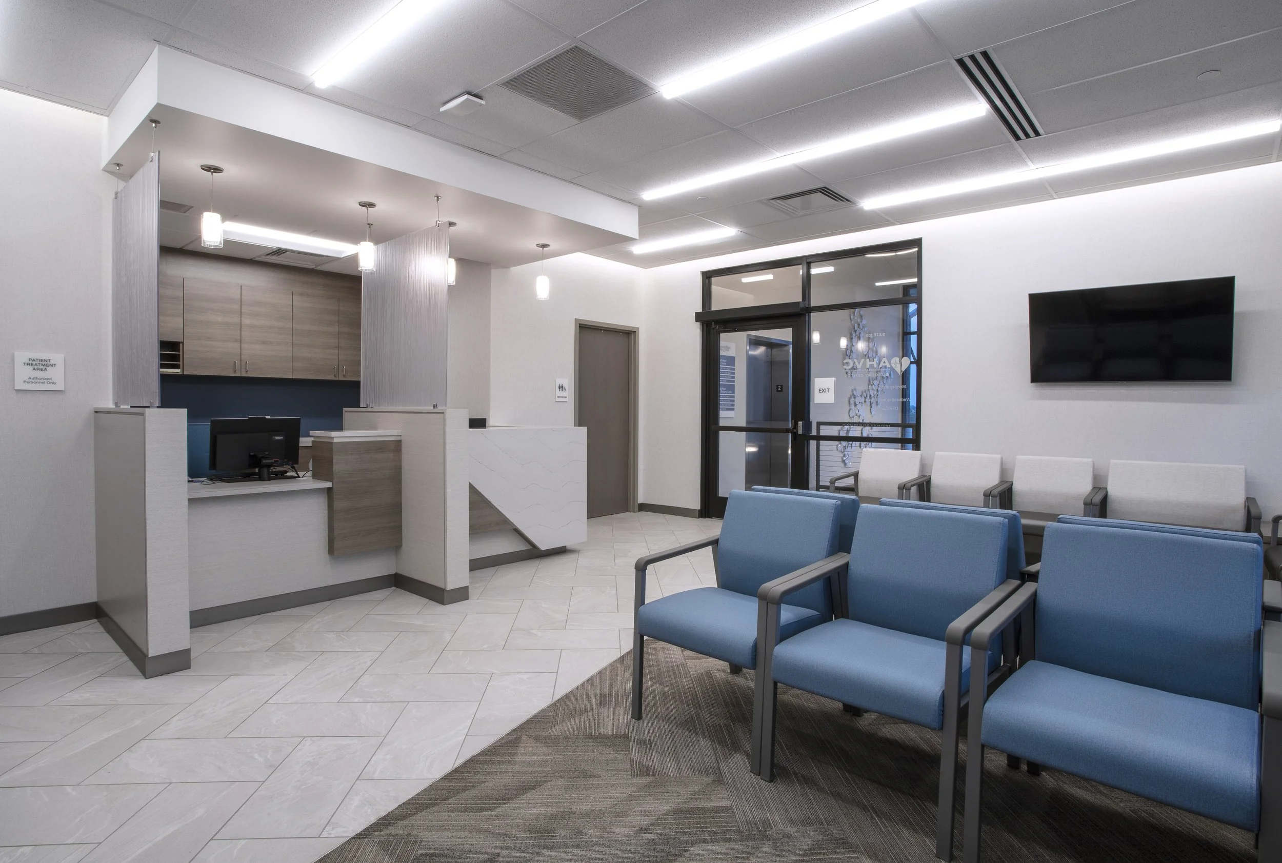 Empty waiting room with blue chairs, reception desk, and waiting area in a modern medical facility.