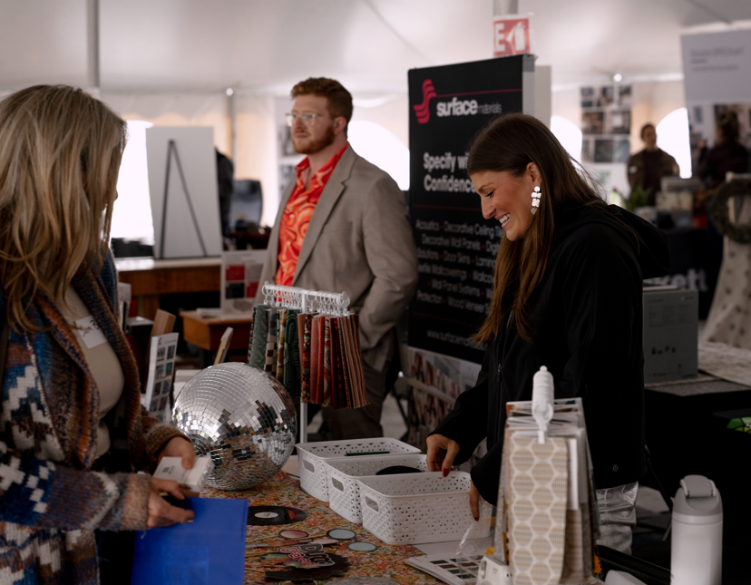 People browsing at an indoor market or trade fair with a table displaying various items including a disco ball and sample cards.