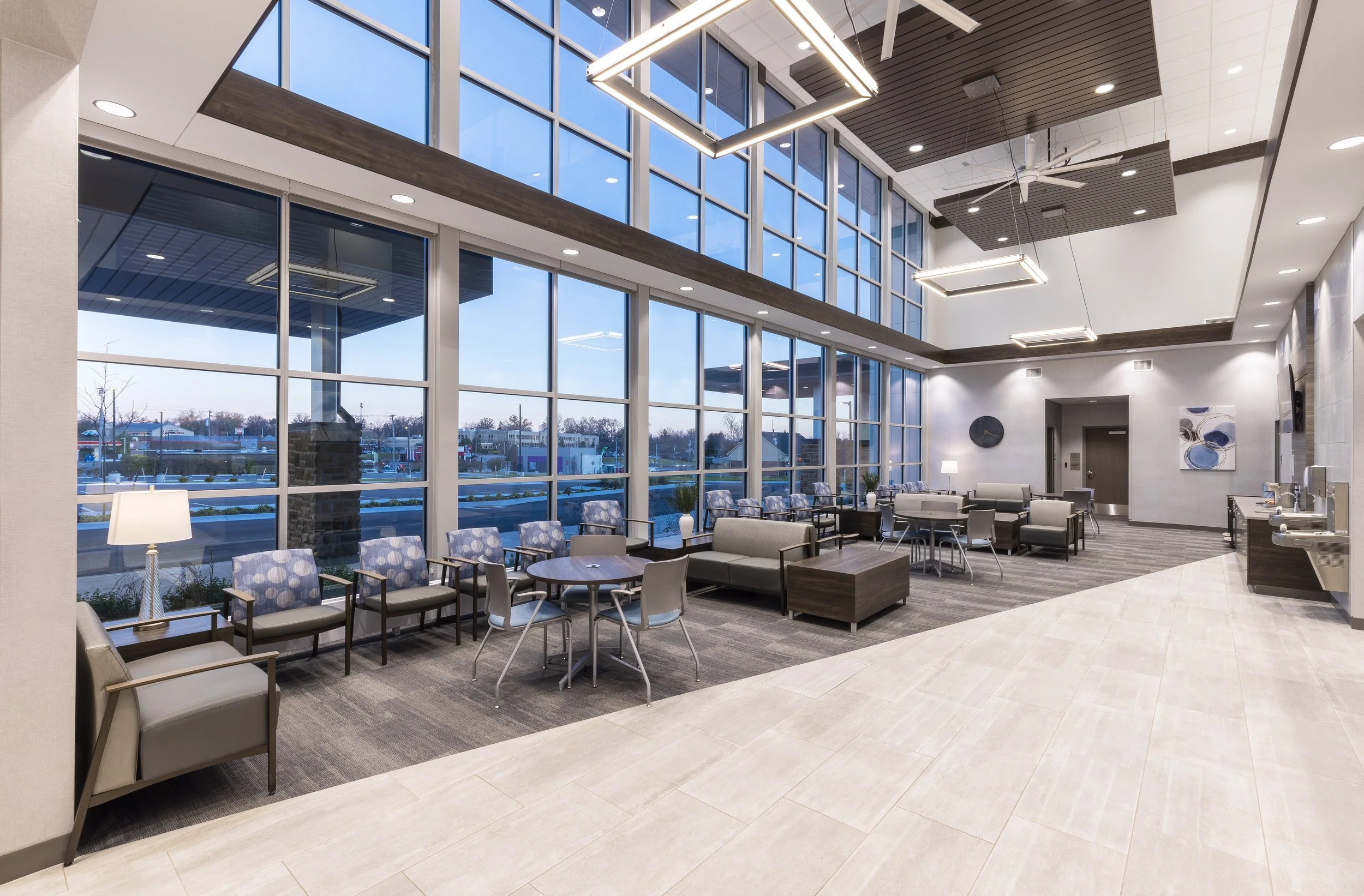 Spacious indoor lounge area with large windows, modern lighting fixtures, and seating arrangements including chairs and sofas.