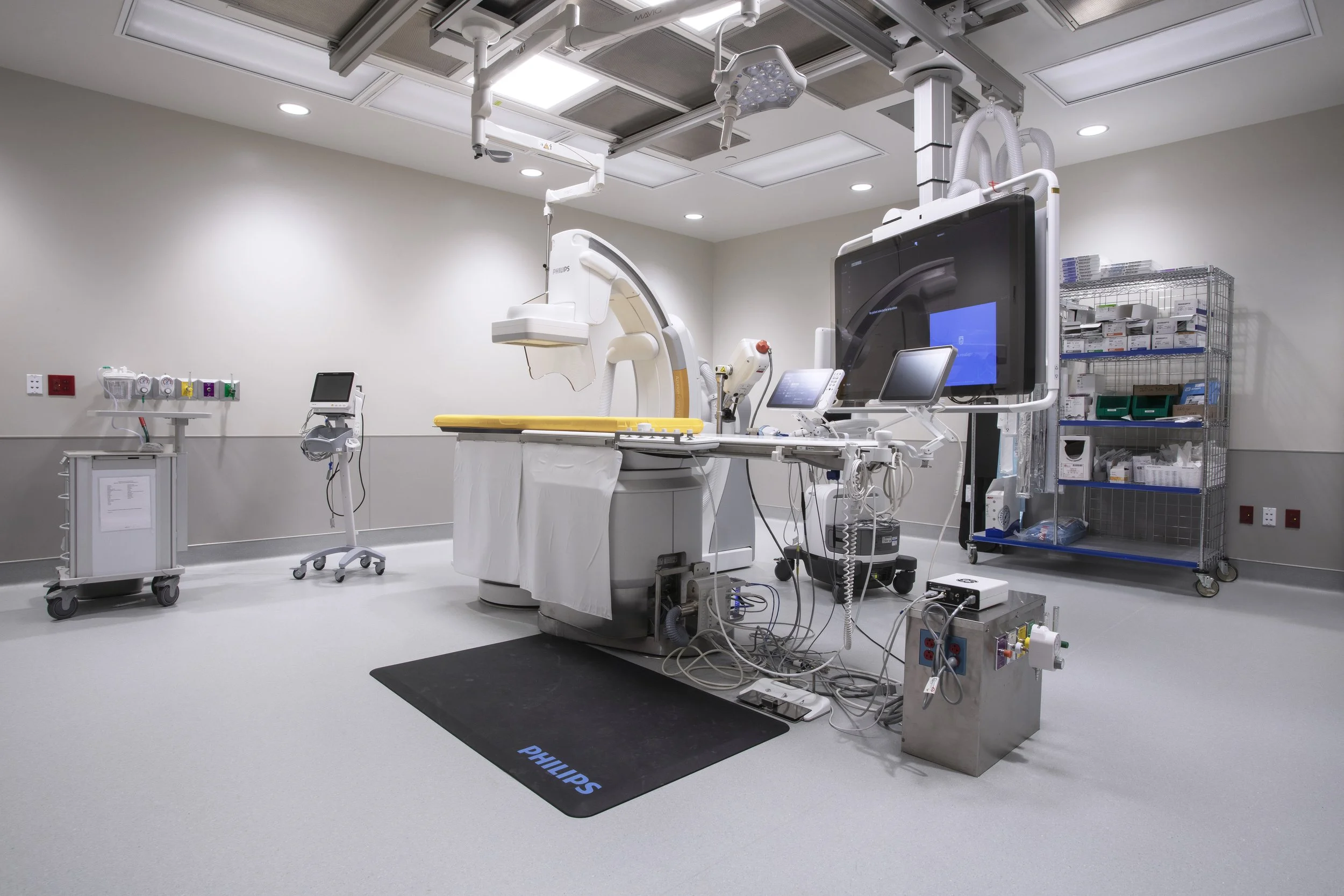 Empty medical operating room with surgical equipment, monitors, and a hospital bed with a yellow mattress, clean and sterile environment with overhead lights