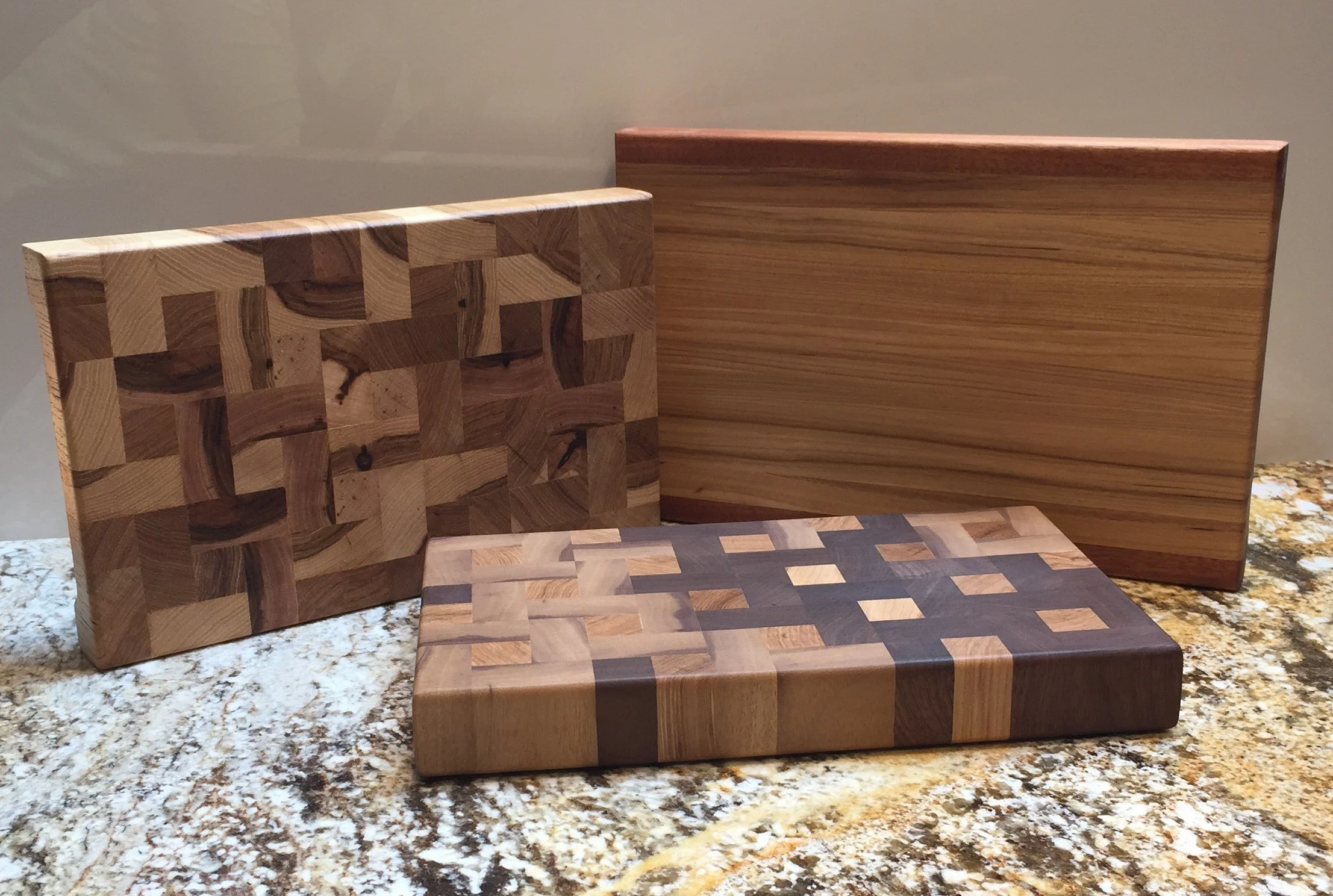 Various wooden cutting boards with different geometric patterns and finishes, placed on a granite countertop.