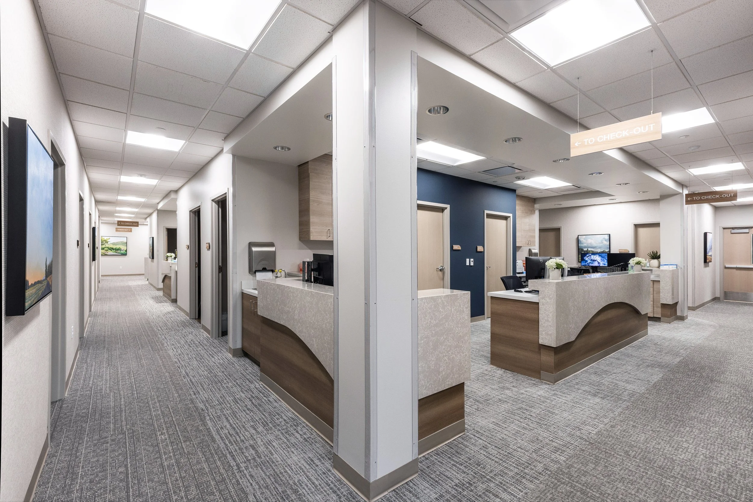 Interior of a modern healthcare or office facility with a reception area, corridor, and signs indicating the way to check-out.