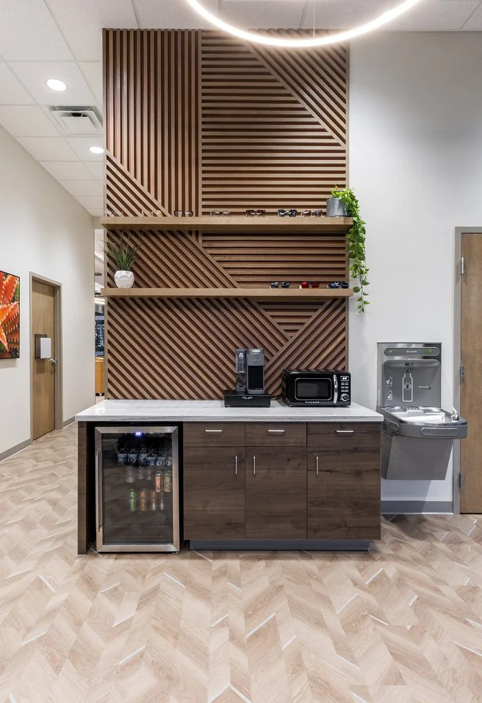 Coffee station with a wooden lattice wall, two shelves with vases and plants, a mini fridge, coffee maker, microwave, and water dispenser.