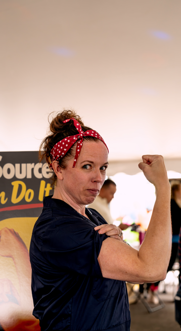 Woman with a red polka dot headband flexing her right arm showing her bicep at an indoor event.