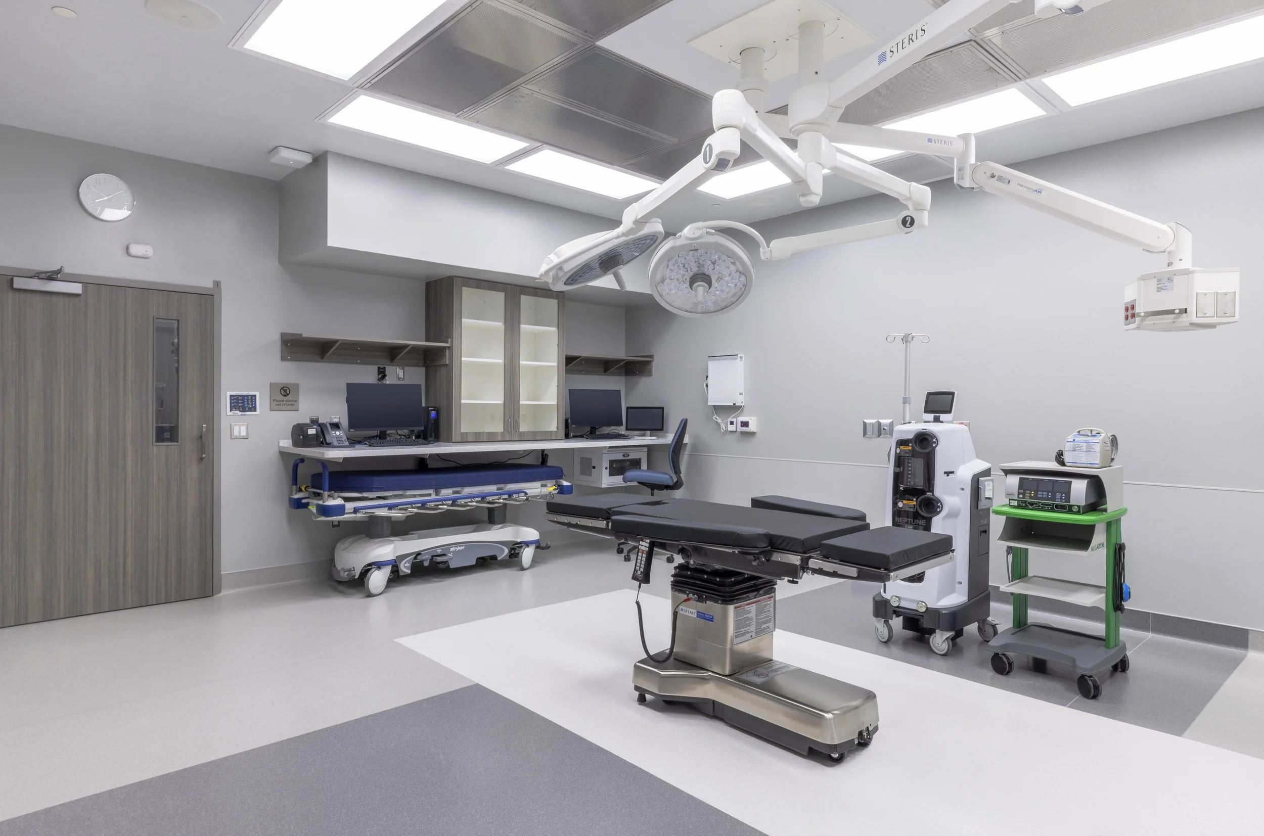 An empty hospital operating room with medical equipment, a hospital bed, surgical lights, monitors, and other medical devices.