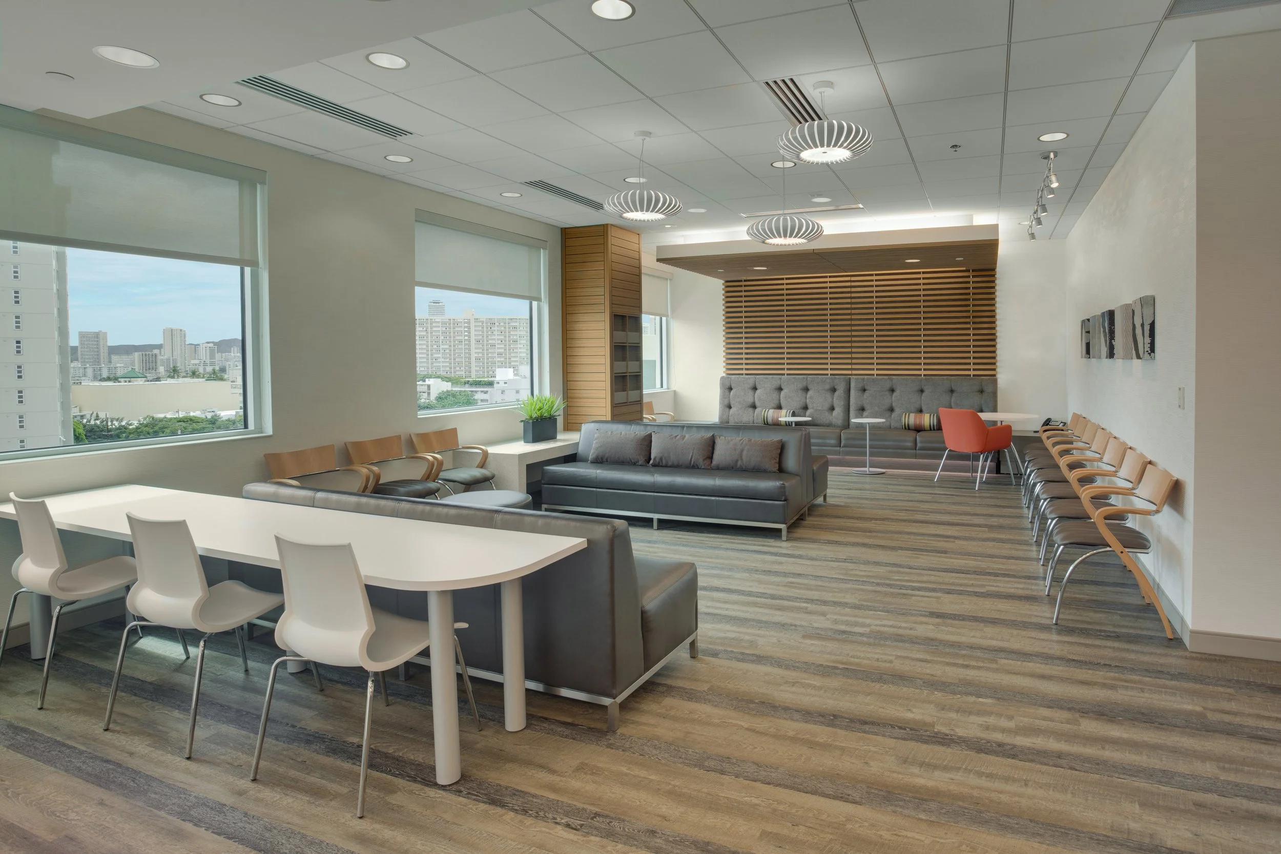 Modern office lobby with large windows, seating area with sofas and chairs, wooden panels on the walls, pendant lights, and city view.