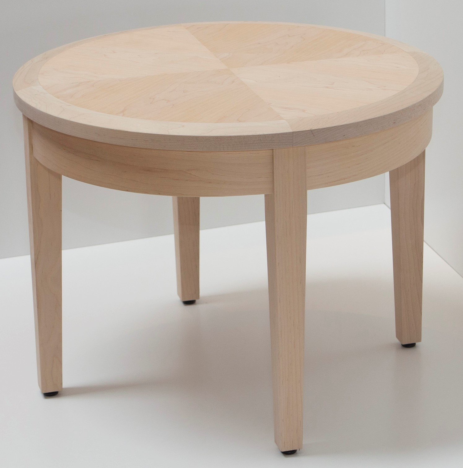Light wooden round side table with four legs, set on a white surface against a white background.