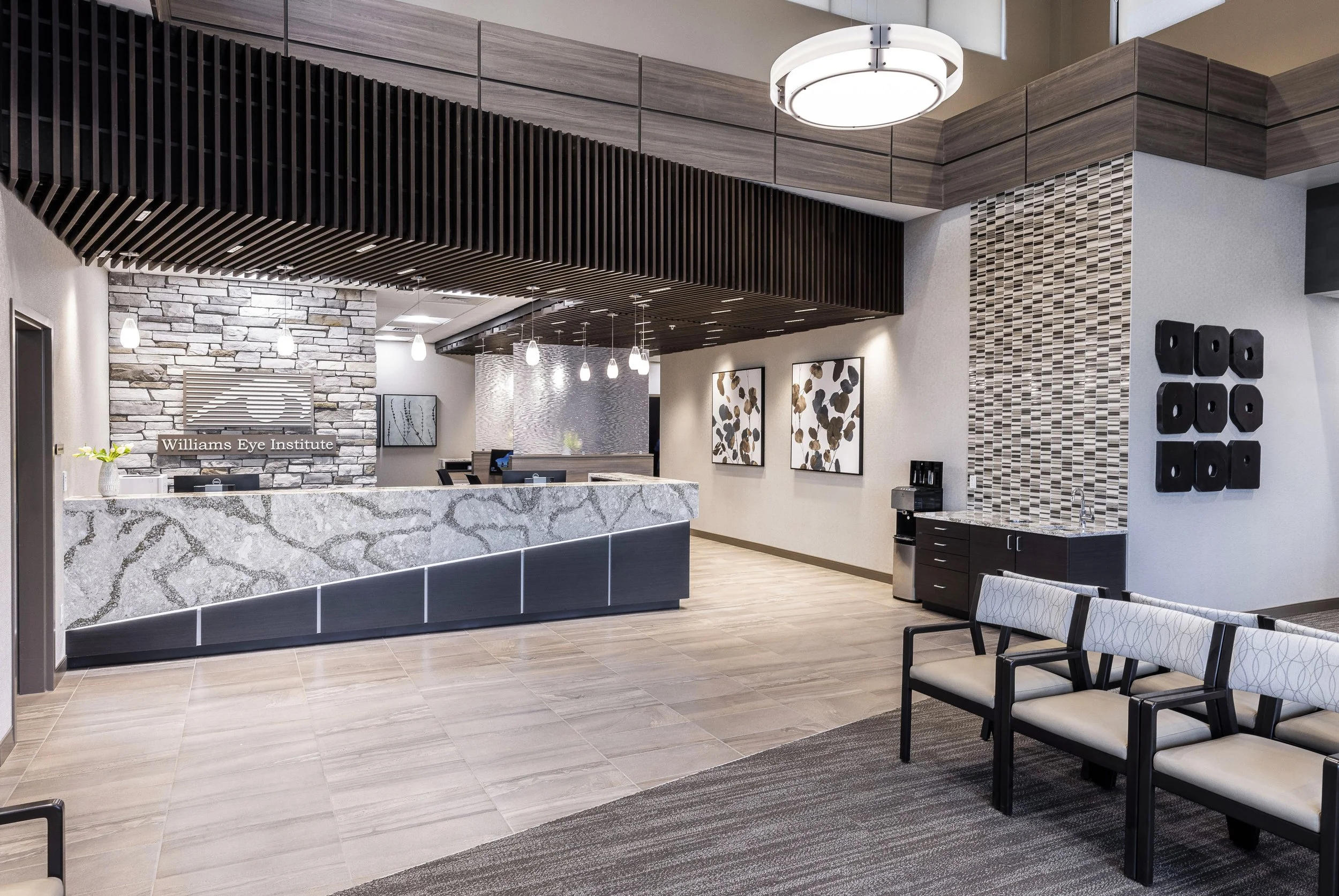 Modern waiting area at Williams Eye Institute with a reception desk, stone accent wall, artwork, black and white chairs, and decorative lighting.