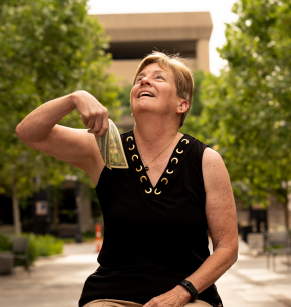 A woman outdoors smiling and holding a wad of cash in her hand.