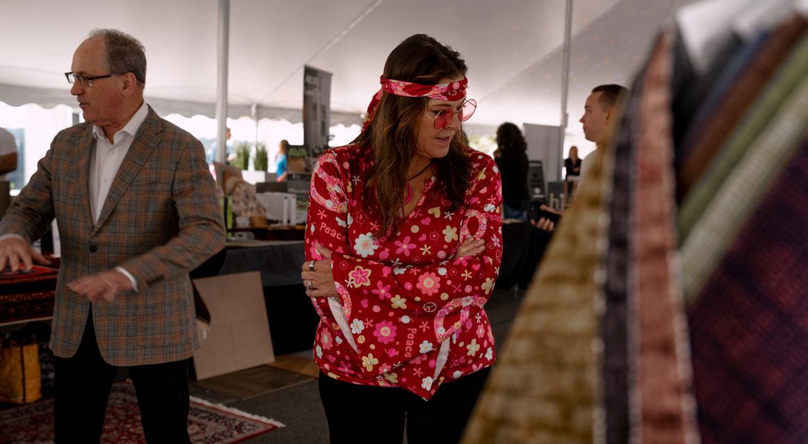 Woman dressed in 1960s hippie fashion browsing through colorful tie-dye and patterned fabric at an indoor market.