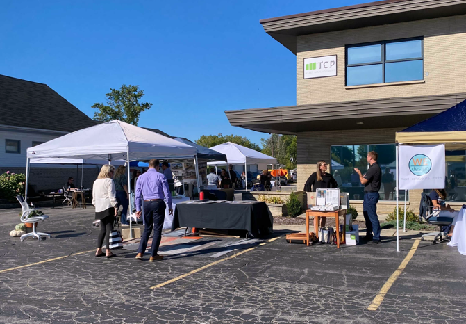 Outdoor business event with tents, tables, and people talking in a parking lot on a sunny day.
