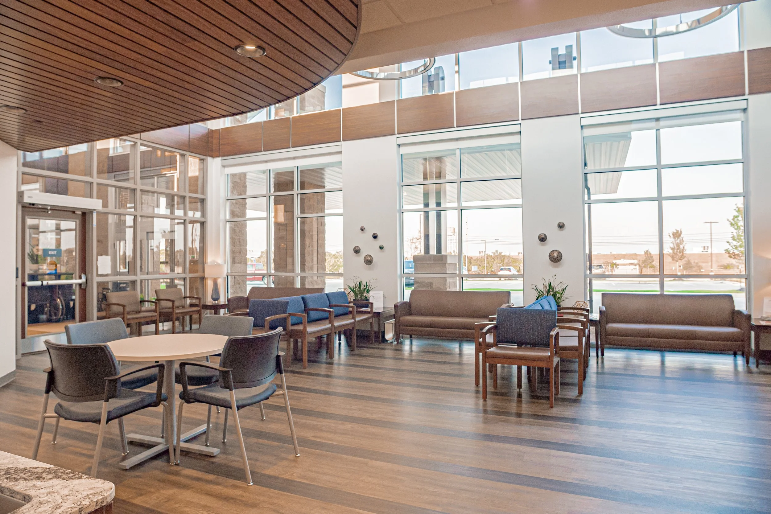 Interior of a modern lobby or waiting area with large windows, wooden accents, and seating including chairs and sofas.
