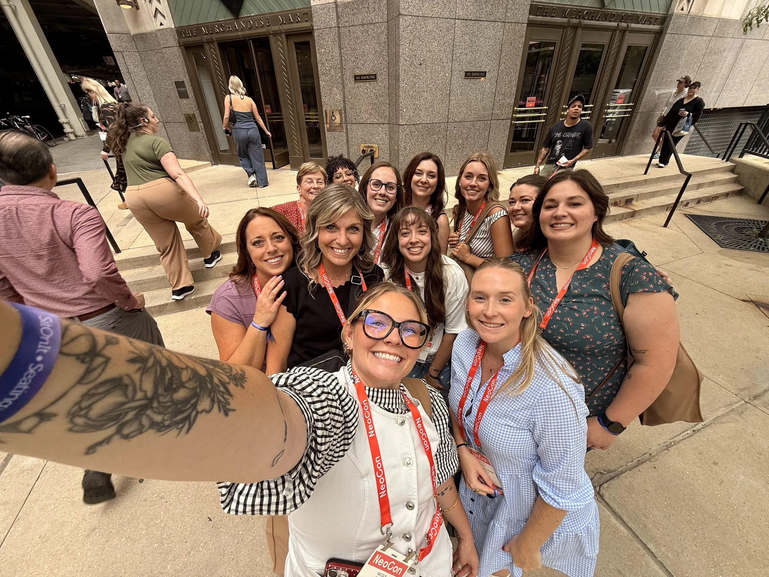 Group of women taking a selfie in front of a building with steps, holding food and wearing conference badges.