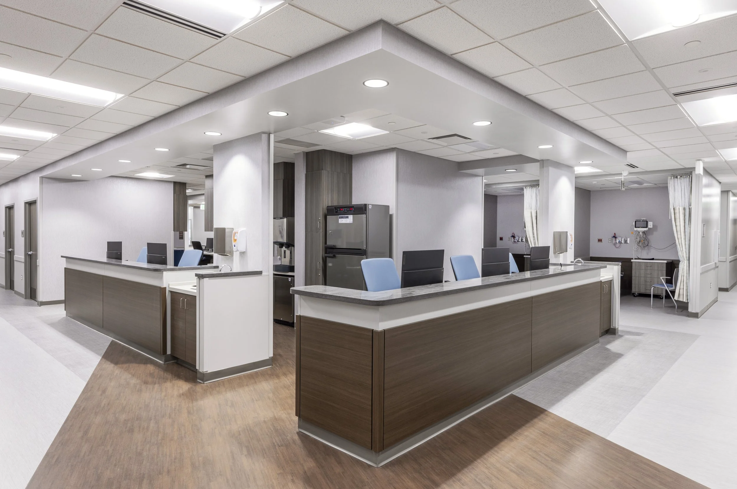 Modern hospital nurse station with multiple computer monitors, wooden cabinets, and medical equipment in a bright, clean environment.