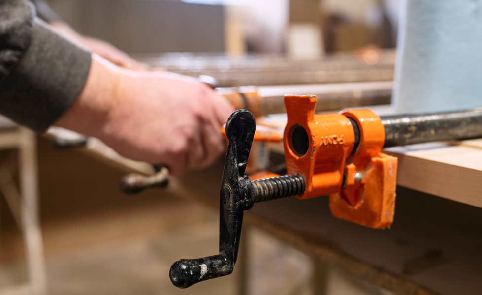 Close-up of a woodworking clamp securing a piece of wood to a workbench.