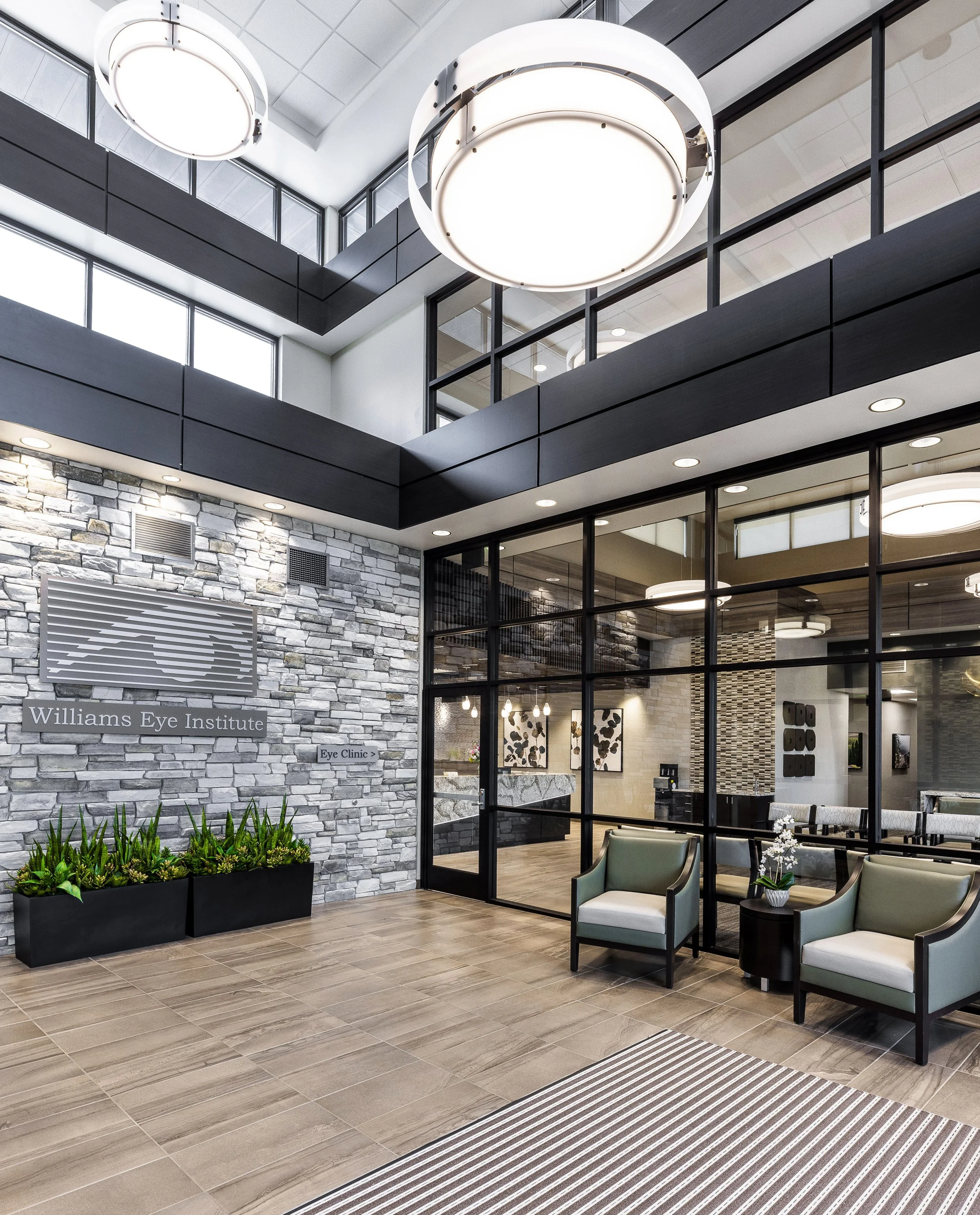 Interior of a modern eye clinic lobby with seating, a stone accent wall, and large circular ceiling lights.