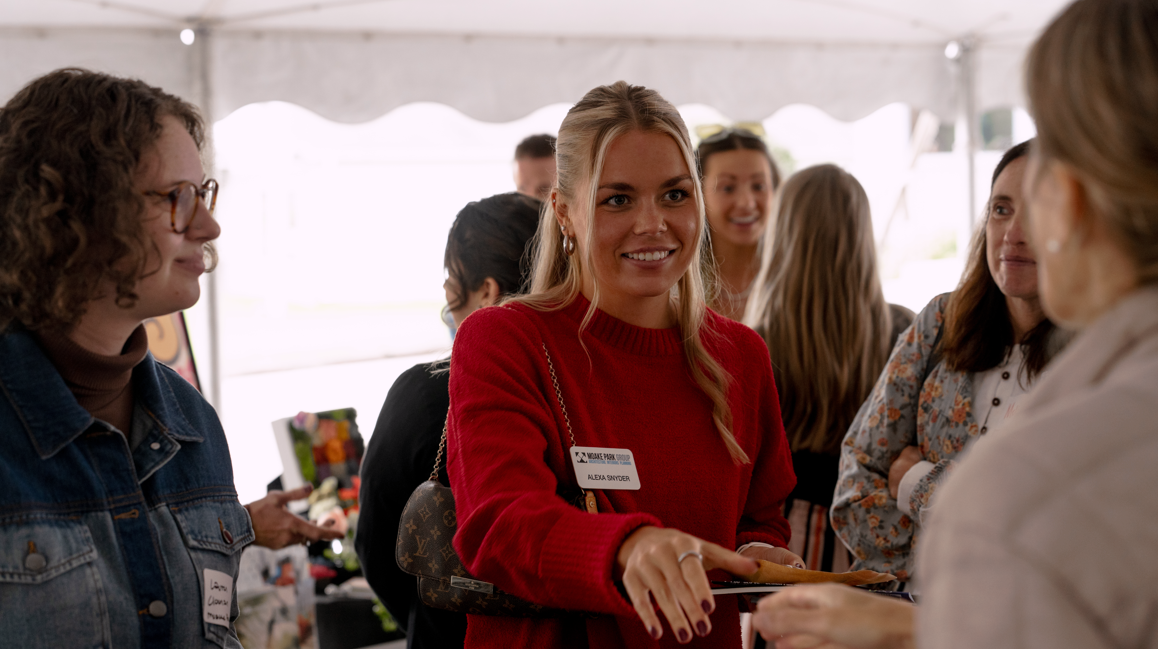 Young woman in red sweater talking and smiling at an event tent.