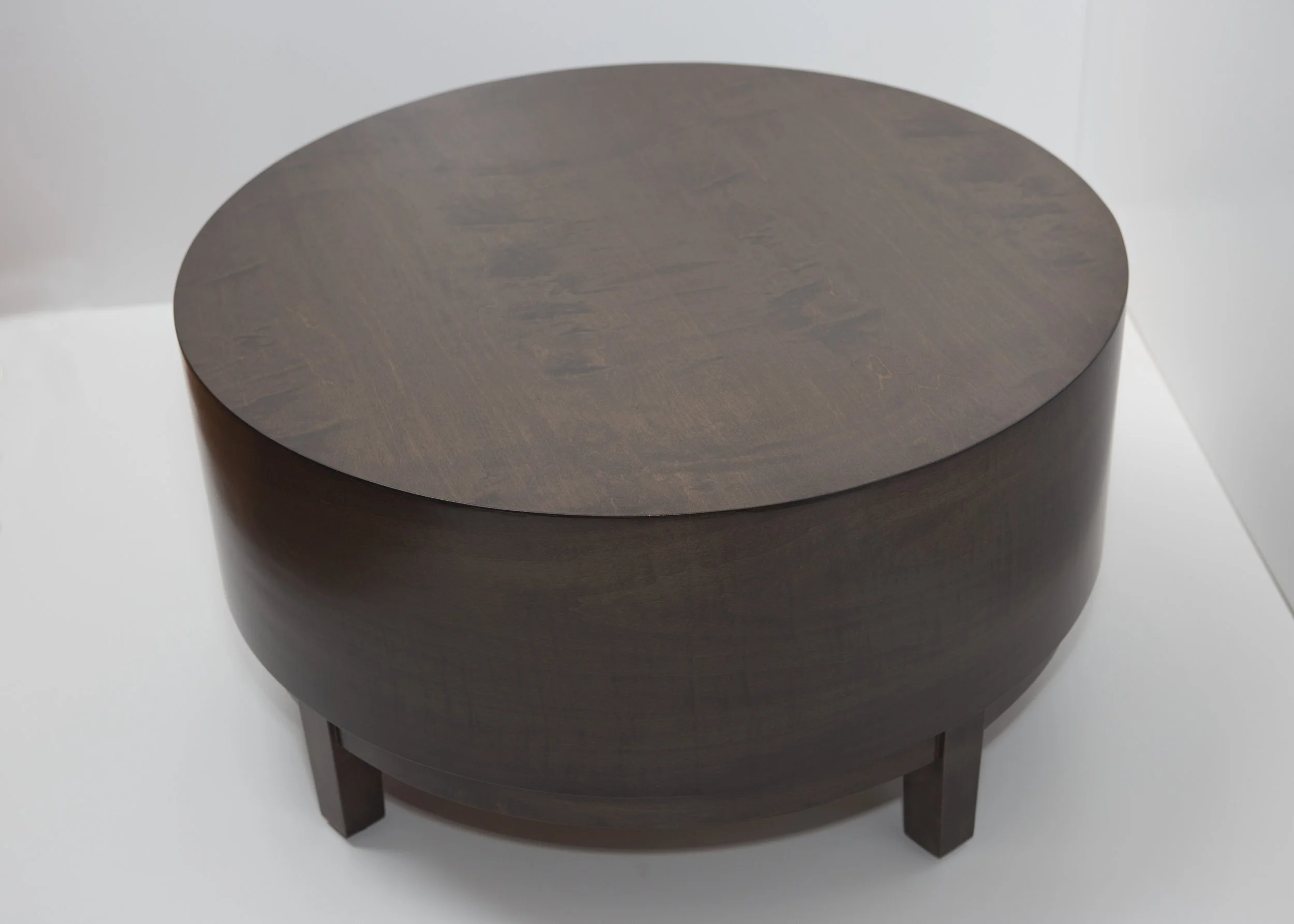 Dark wooden round side table with four legs on a white surface.