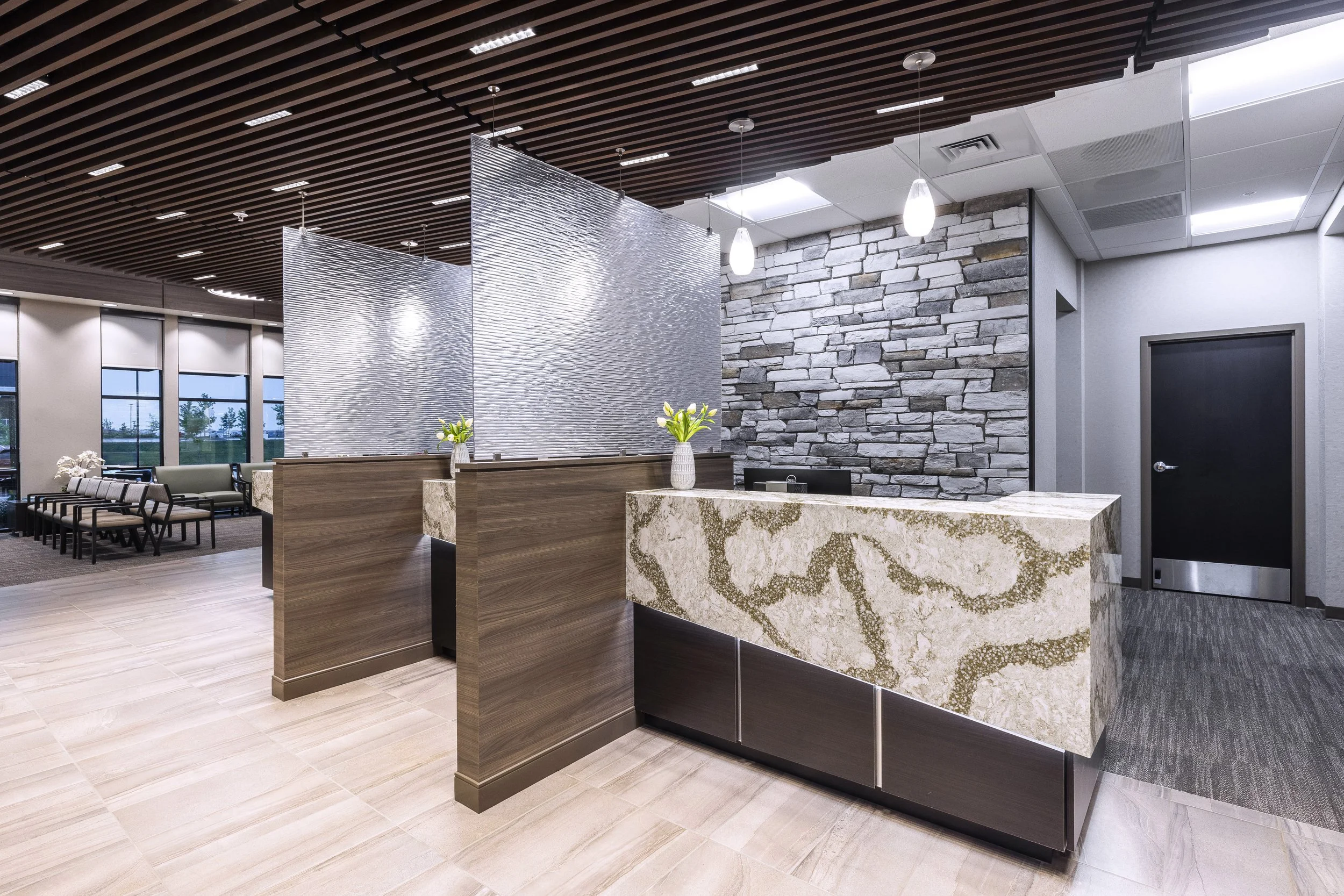 Modern office lobby with stone brick accent wall, a marble reception desk, hanging pendant lights, and wood slat ceiling panels.