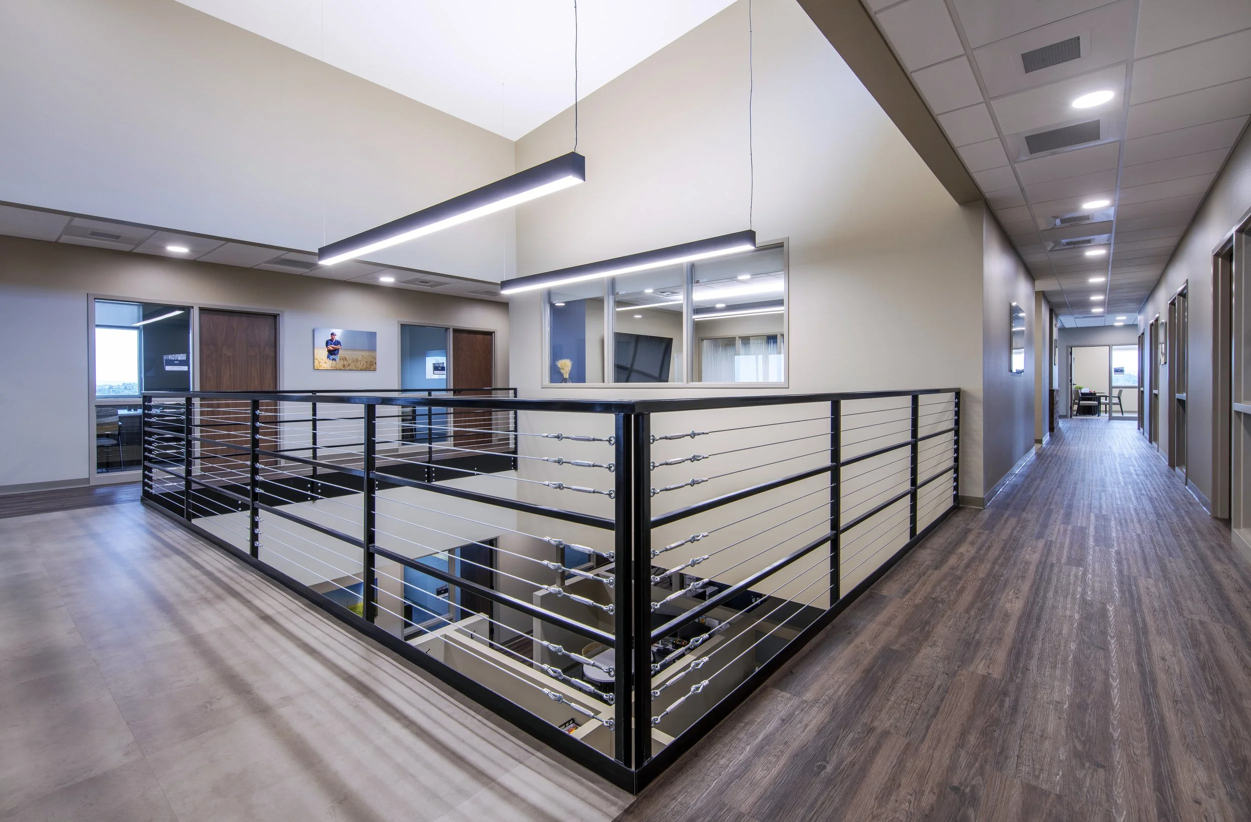 Interior of a modern office building with hallway, glass windows, artwork on walls, and a staircase with metal railing.