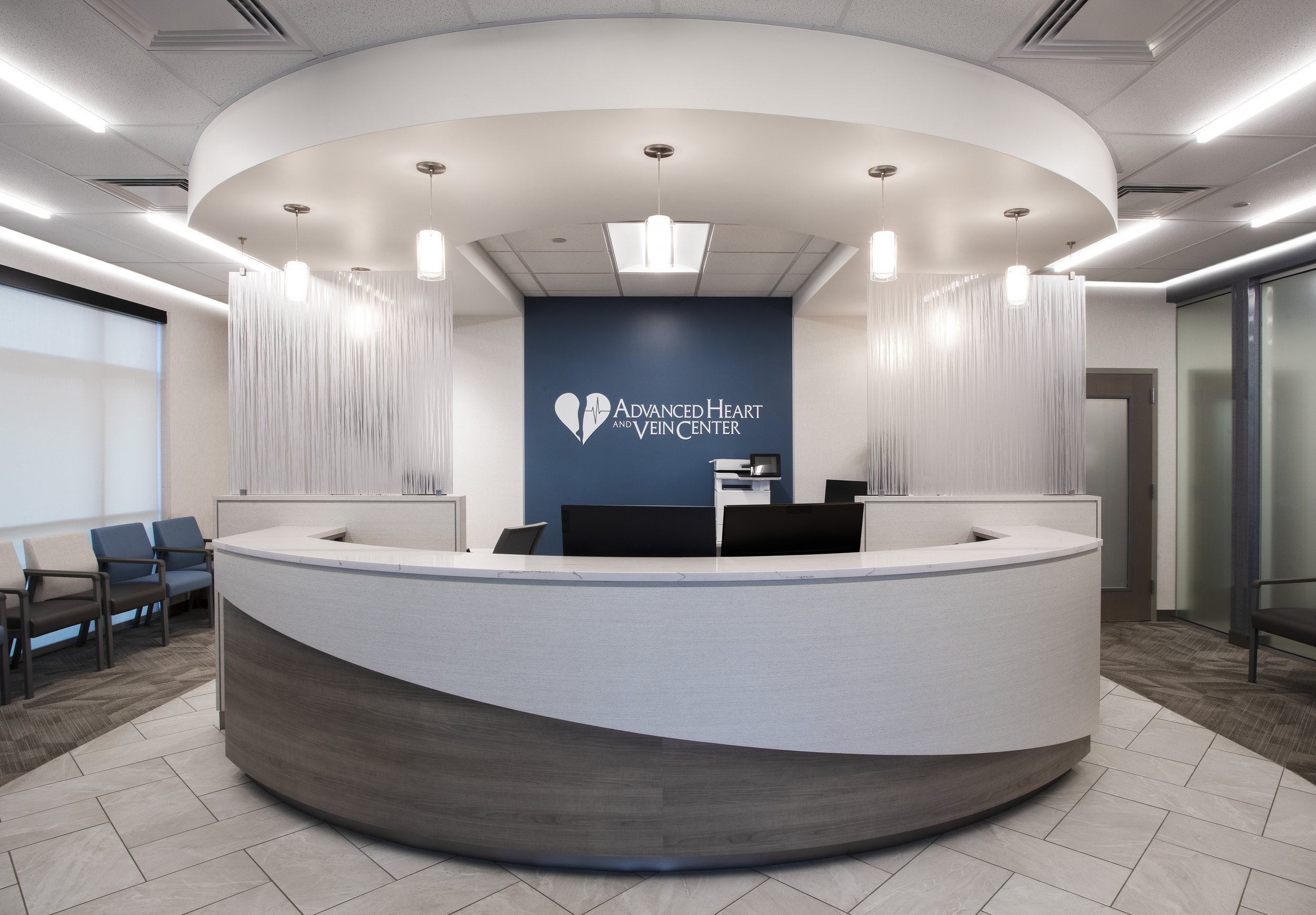 Reception area at a medical center with a curved counter, waiting chairs, and a wall displaying the logo 'Advanced Heart and Vein Center'.