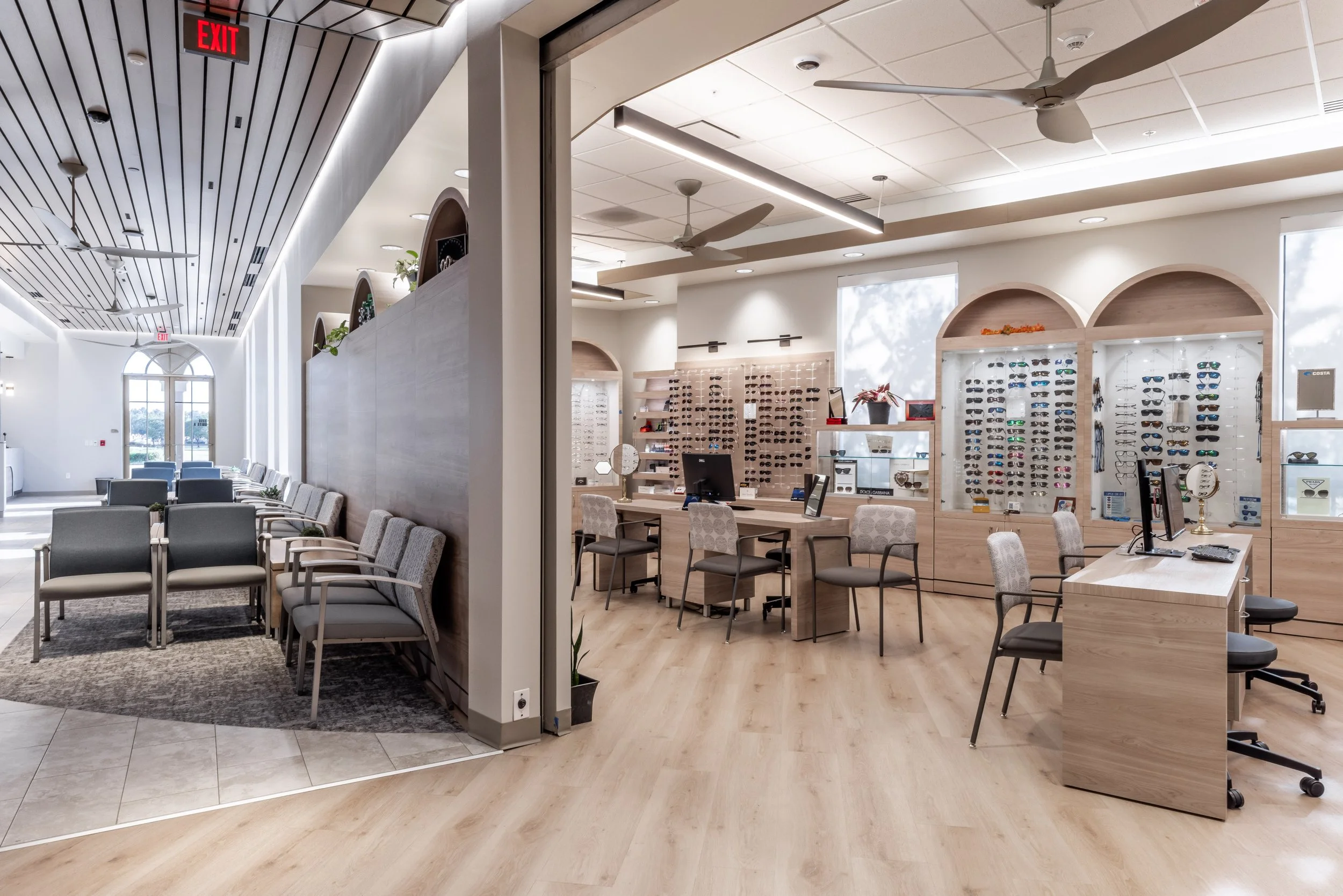 Interior of a retail store with displays of sunglasses, desks, chairs, and ceiling fans in a bright, modern space.